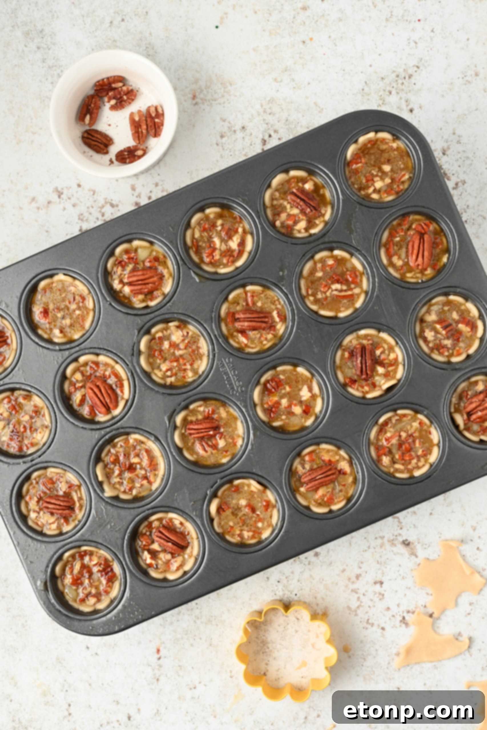 An overhead shot showcasing a batch of freshly baked mini pecan pies, still nestled in their baking tray, their golden tops glistening.