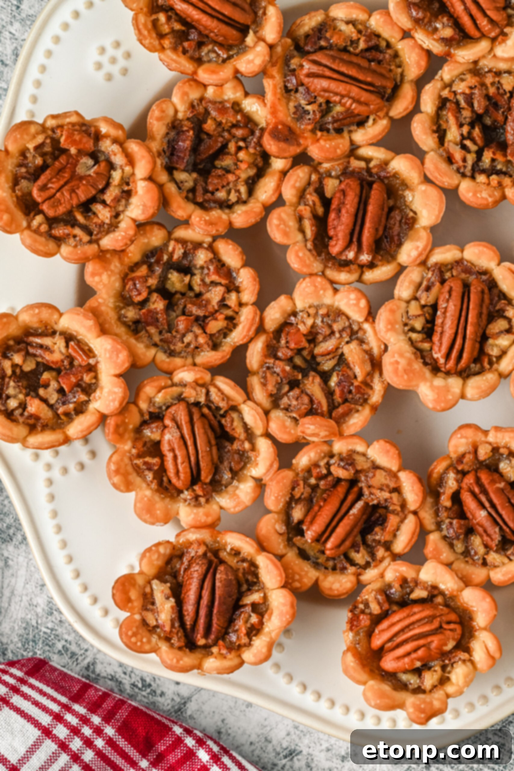 A pristine overhead view of mini pecan pies artfully arranged on a clean white serving tray, highlighting their perfect golden finish.