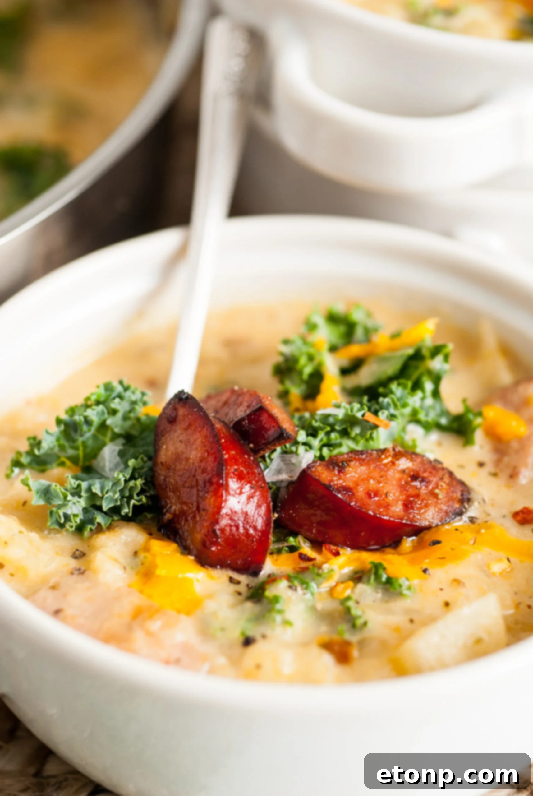 A bowl of Kielbasa Potato Soup, garnished with fresh kale and additional kielbasa, on a rustic wooden table.