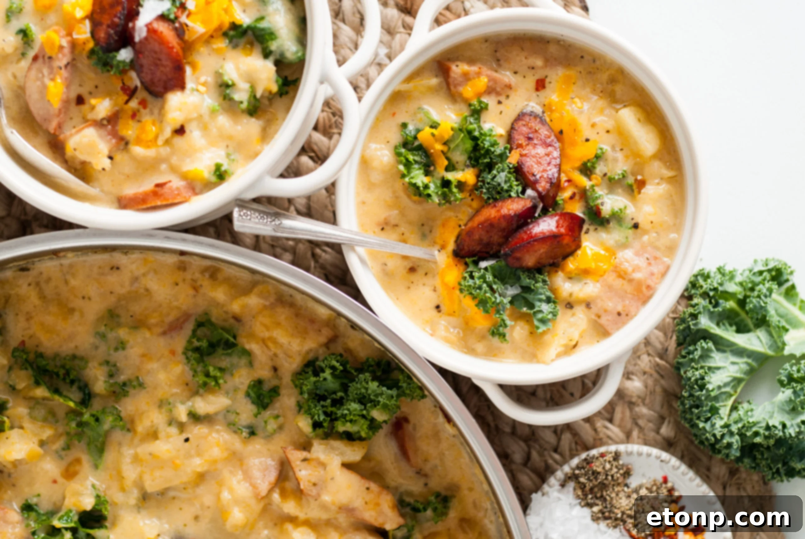 Overhead shot of two white bowls of Kielbasa Potato soup, garnished with fresh kale and cooked kielbasa slices.