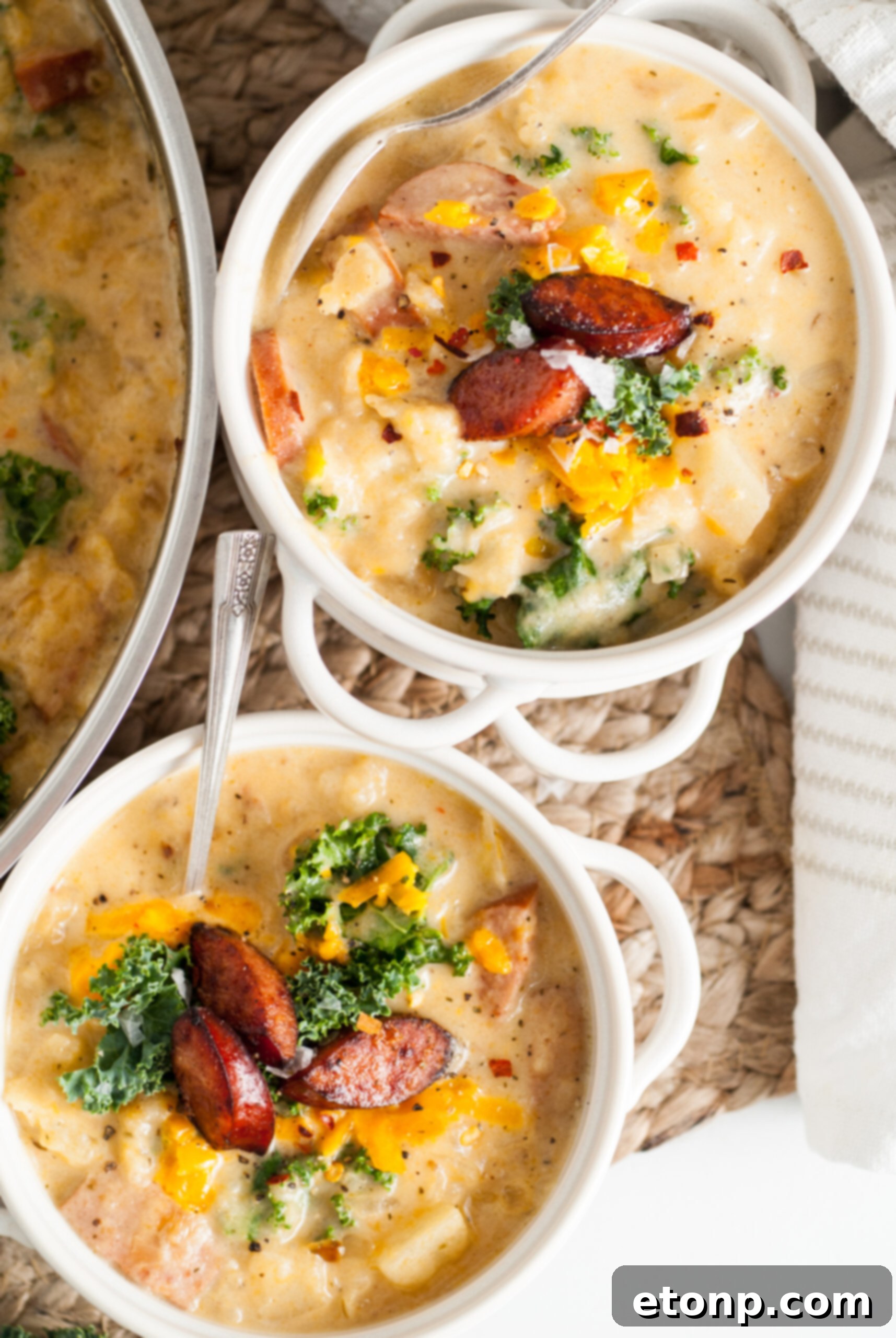Overhead shot of two white bowls of Kielbasa Potato soup, garnished with fresh kale and cooked kielbasa slices, in a slightly different angle.