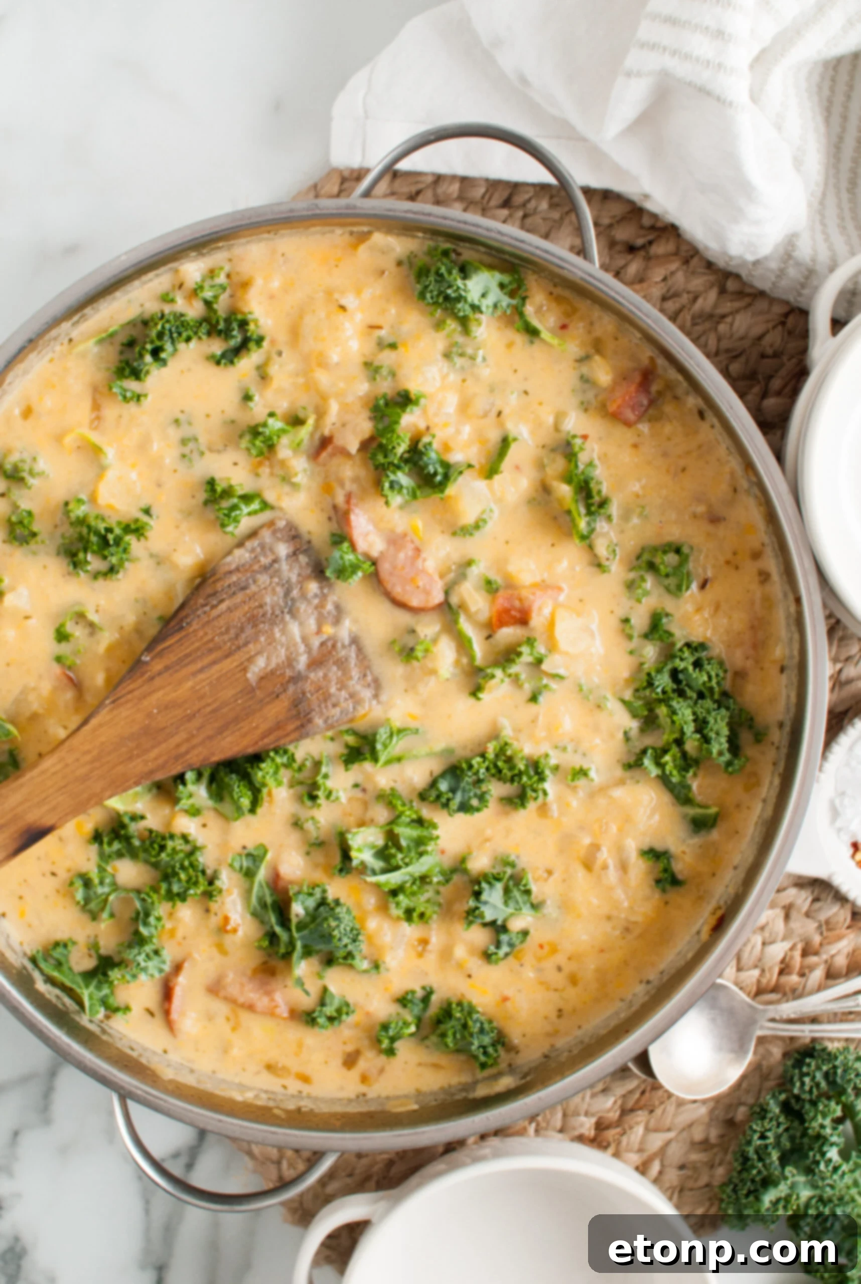 Overhead shot of creamy Kielbasa Potato soup simmering in a silver skillet, garnished with fresh herbs.