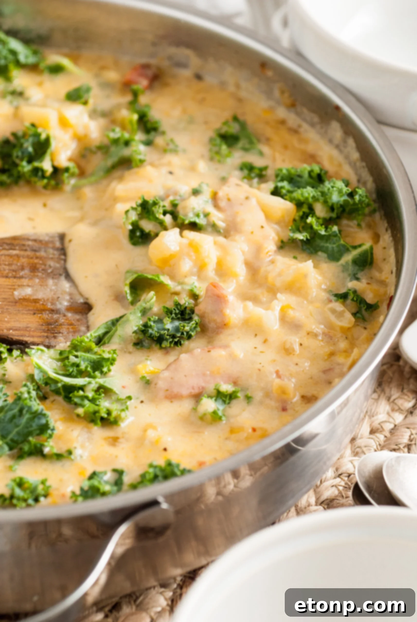 Side shot of creamy Kielbasa Potato soup simmering in a silver skillet, with steam rising.