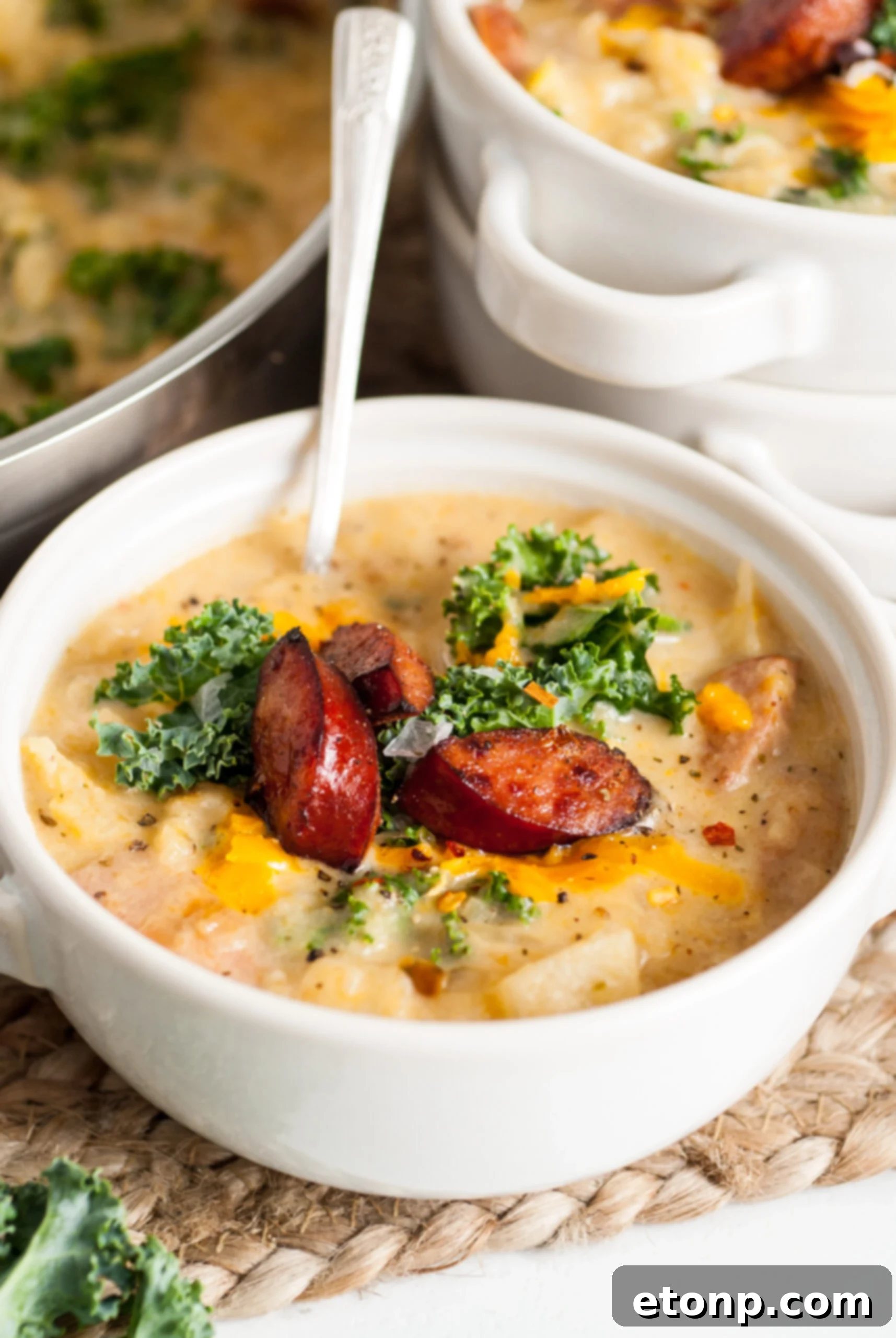 Kielbasa Soup in a white bowl topped with fresh kale and cooked kielbasa slices, ready to serve.