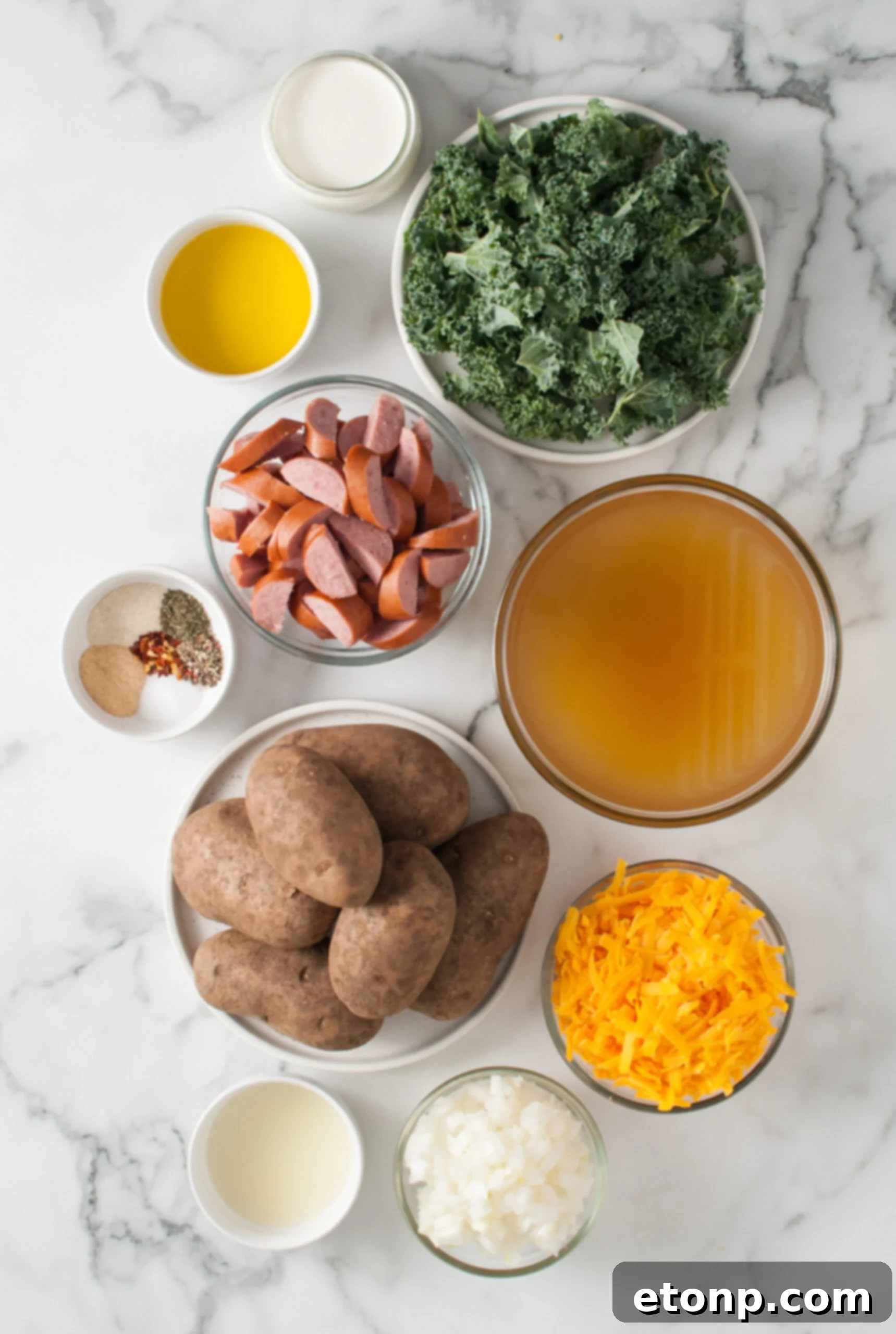 Overhead shot of all fresh ingredients laid out on a wooden surface, including kielbasa, potatoes, cheese, and herbs.