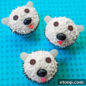 Fluffy polar bear cupcakes with white frosting, marshmallow ears, and a chocolate chip nose, great for winter parties.