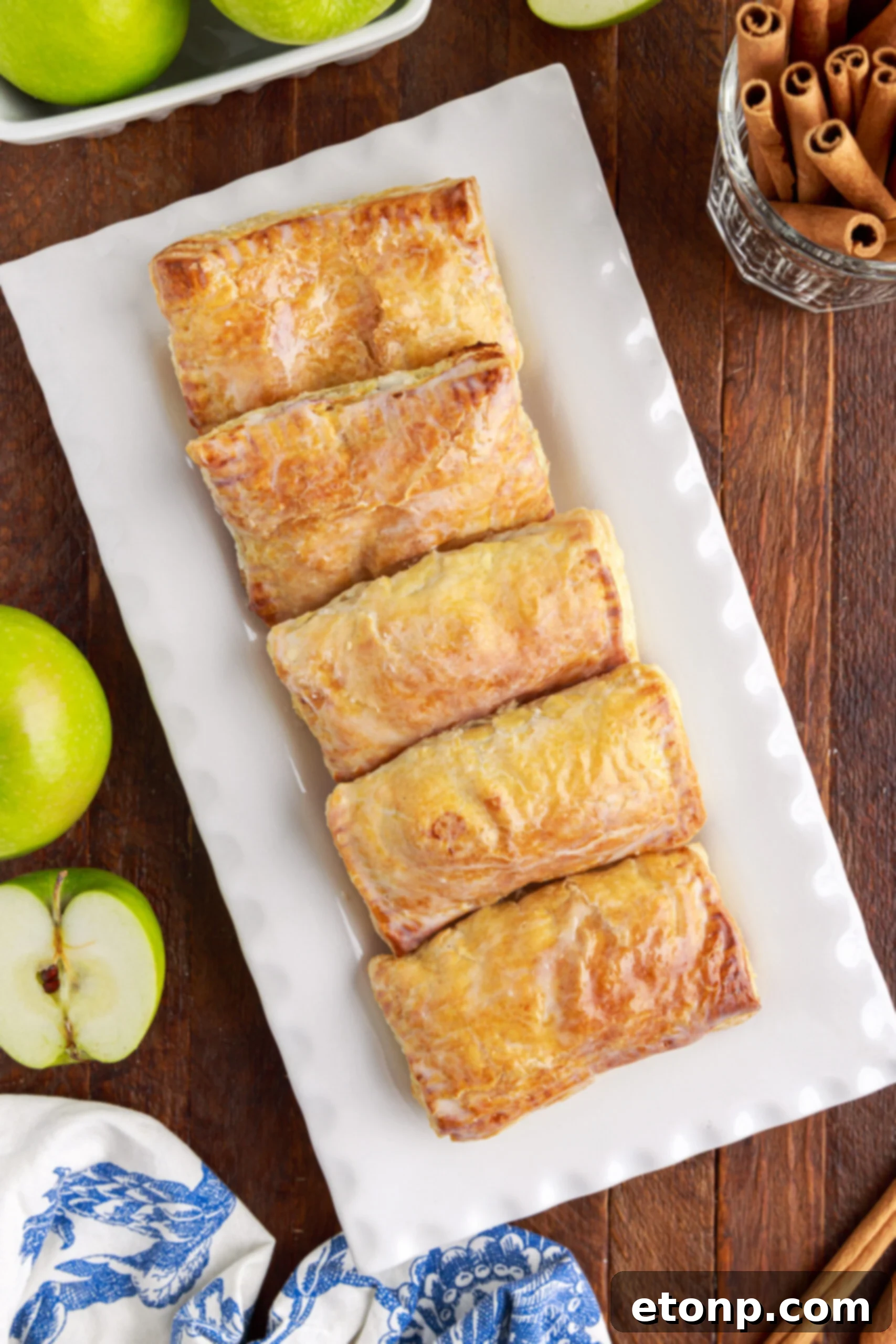 An overhead shot showcasing six golden-brown apple hand pies, beautifully arranged on a pristine white serving platter.