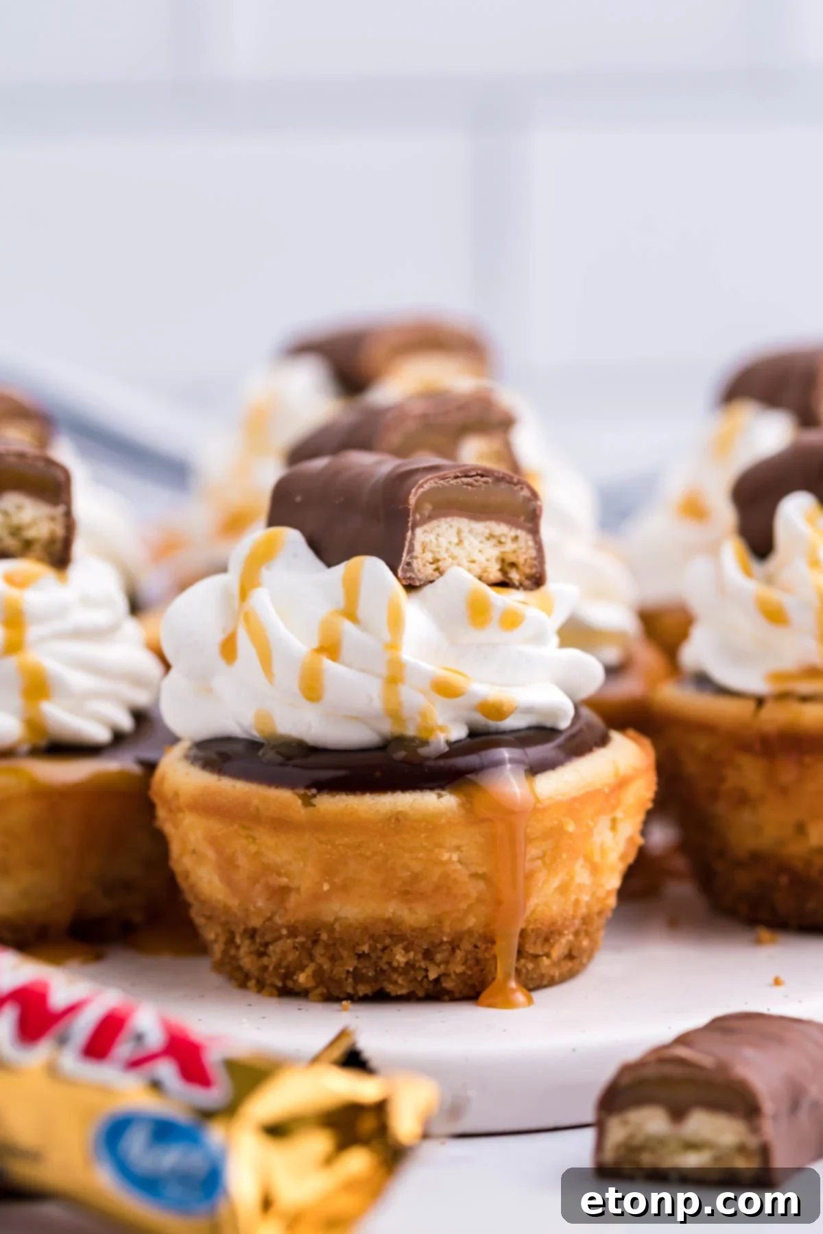 Decadent Mini Twix Cheesecakes 7 Side view of a Mini Twix Cheesecake topped with whipped cream, caramel drizzle, and Twix candy.
