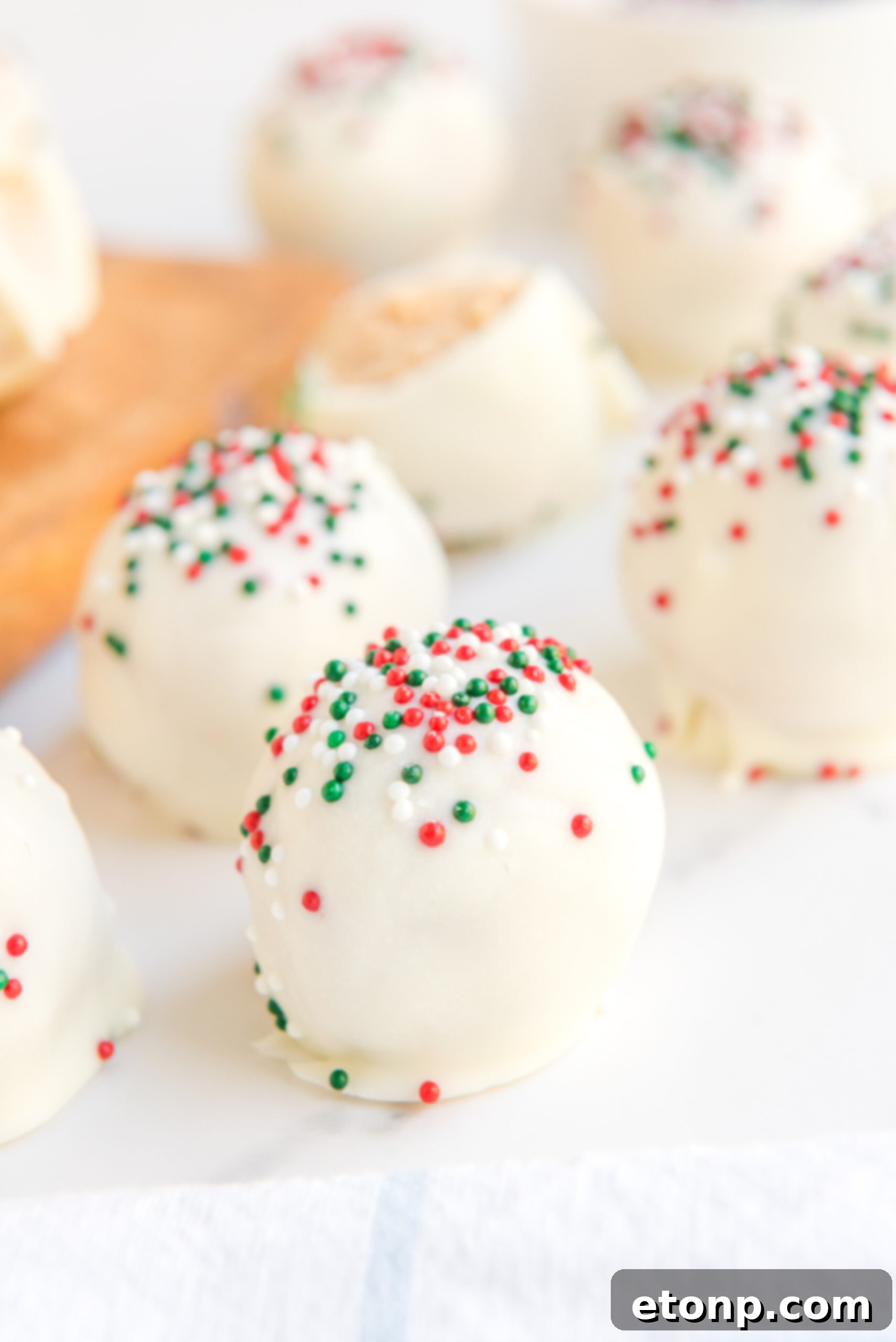Irresistible White Chocolate Peanut Butter Snowballs 3 Close up of white chocolate peanut butter truffles, elegantly topped with festive red, white, and green sprinkles for a holiday touch.