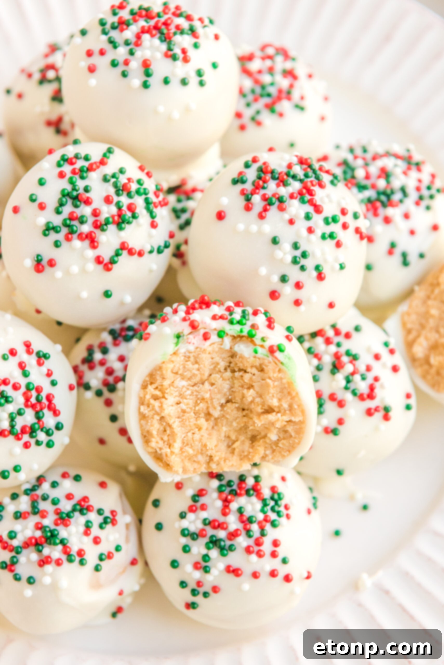 Irresistible White Chocolate Peanut Butter Snowballs 5 A perfectly formed White Chocolate Peanut Butter Snowball, with a small bite taken out, revealing its soft, peanut butter filling on a pristine white plate.
