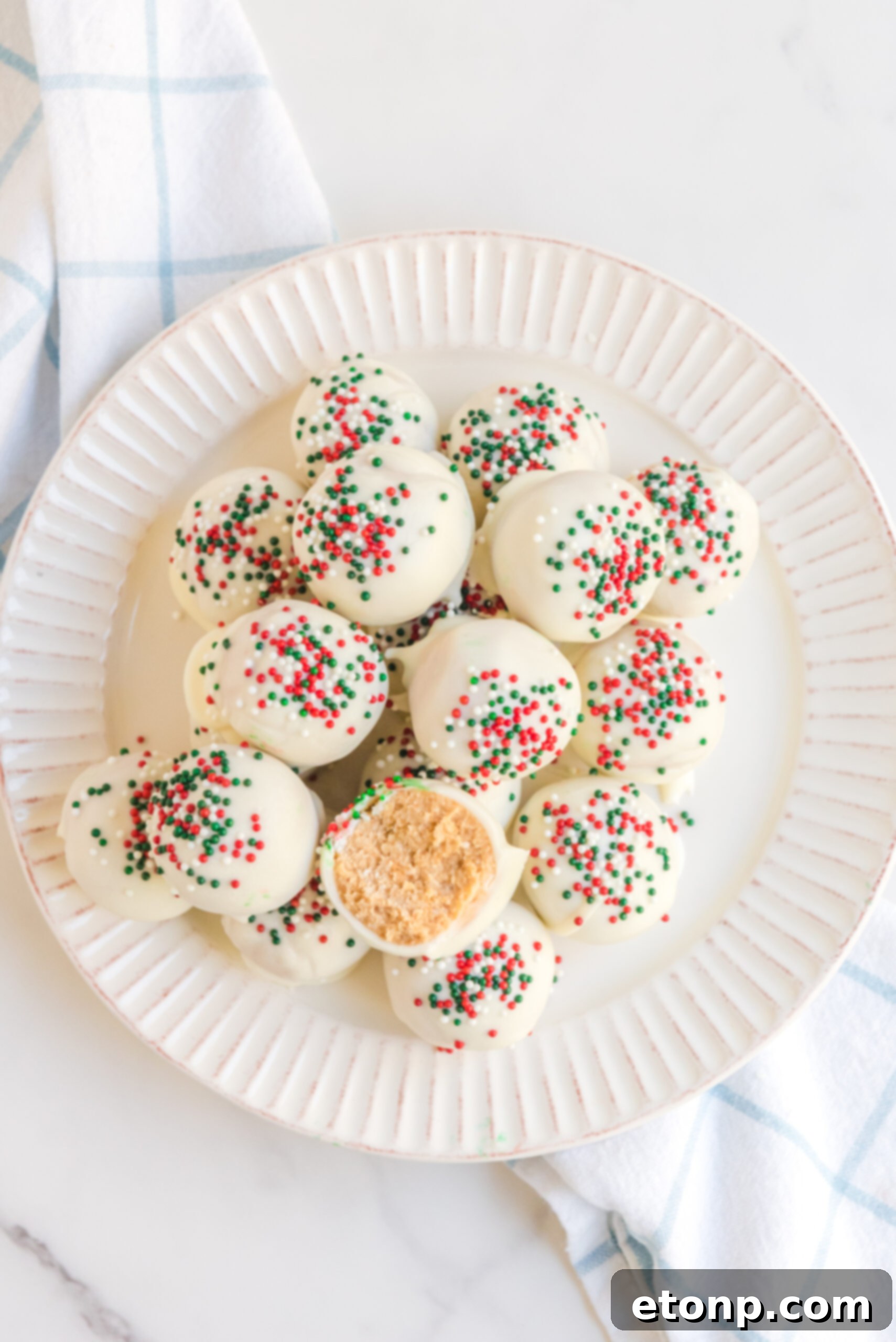 Irresistible White Chocolate Peanut Butter Snowballs 6 An overhead view of a perfectly arranged stack of White Chocolate Peanut Butter Truffles on a white plate, beautifully garnished with festive red, white, and green sprinkles.