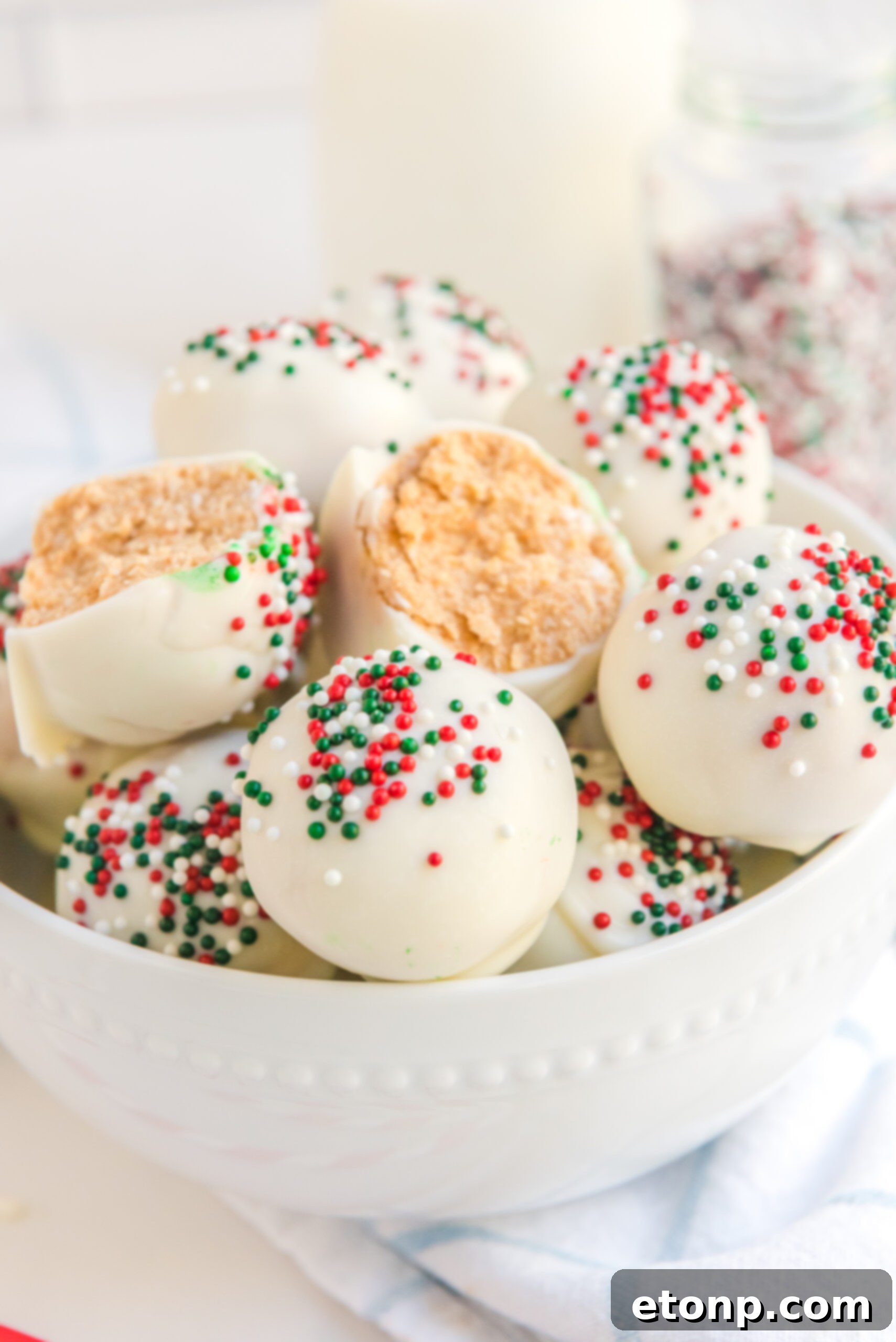Irresistible White Chocolate Peanut Butter Snowballs 8 A White Chocolate Peanut Butter truffle, elegantly cut in half to showcase its creamy interior, stacked on more truffles within a pristine white bowl.