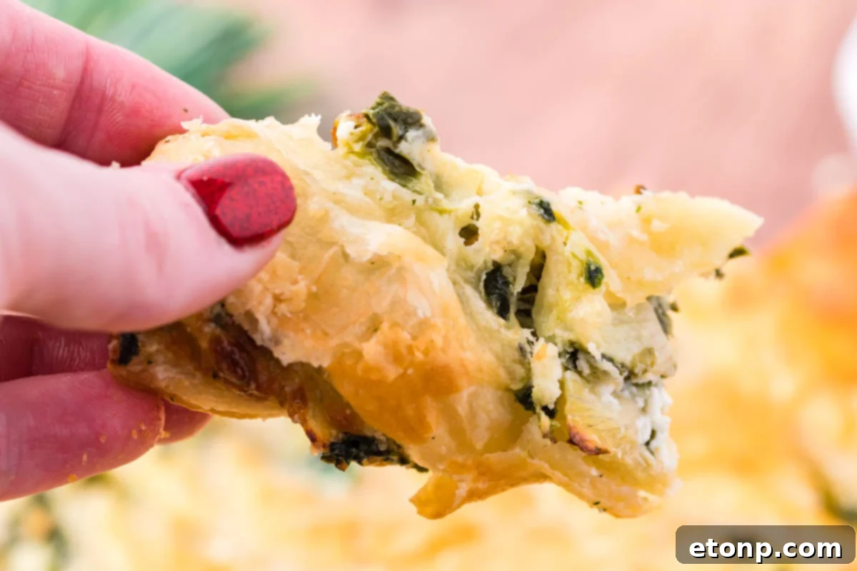 A piece of spinach dip pull apart bread being held up showing the flakey outside layer and spinach dip filling. 