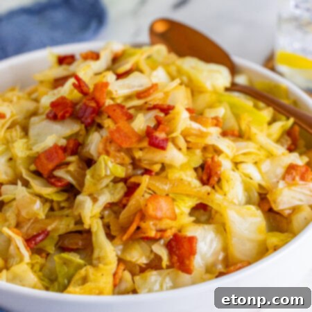 Bacon Fried Cabbage in a white bowl topped with bacon with a gold spoon on the side