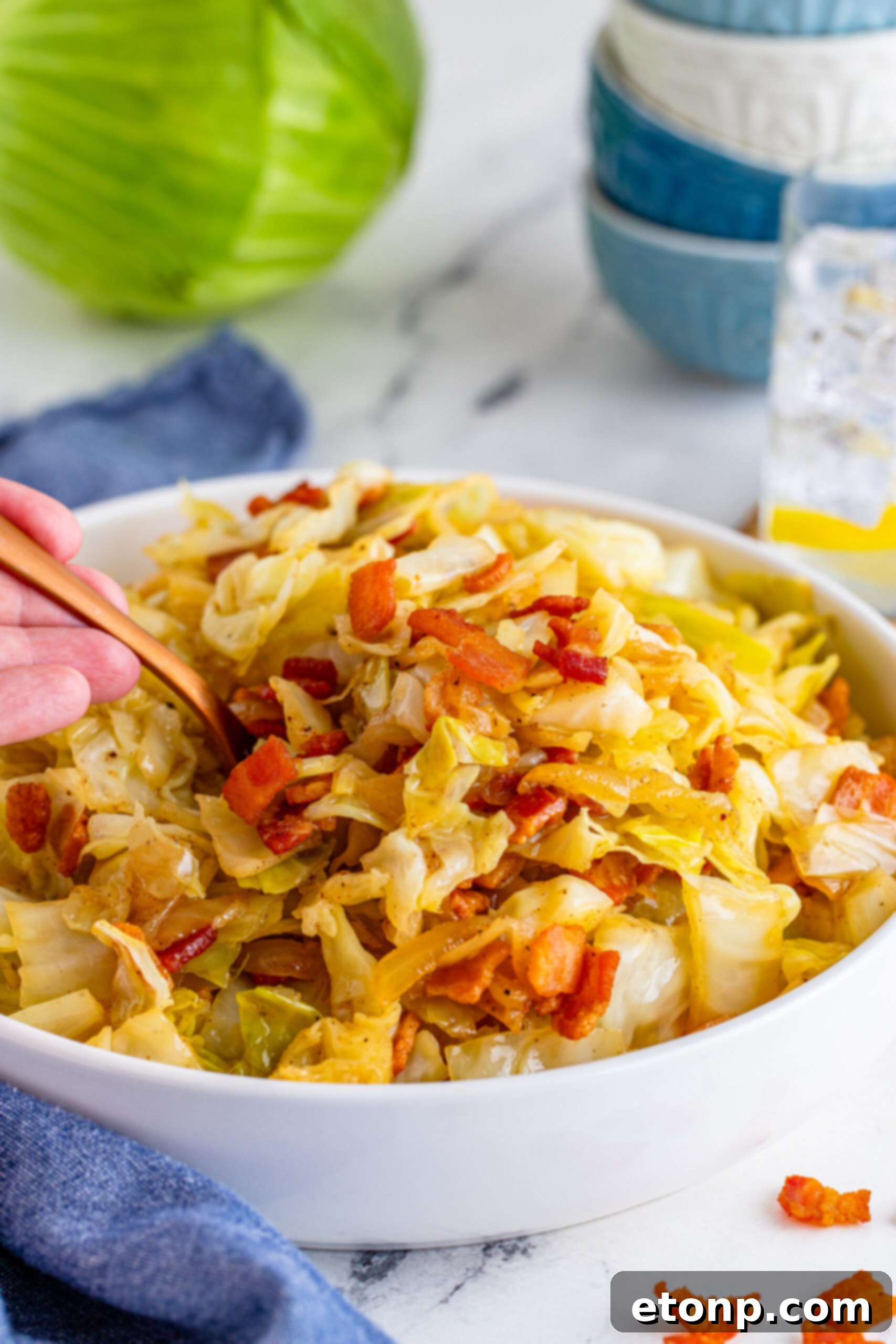Fried Cabbage in a white bowl with a scoop being removed with a gold spoon. 