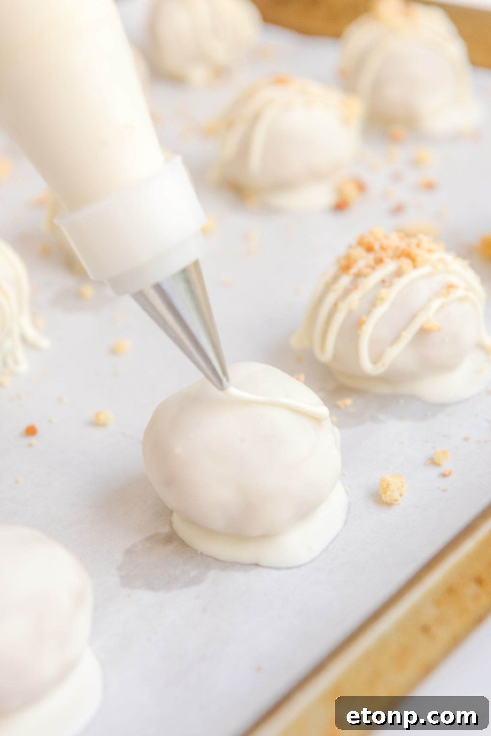 Photo of a piping bag piping on a white chocolate drizzle on top of each truffle.