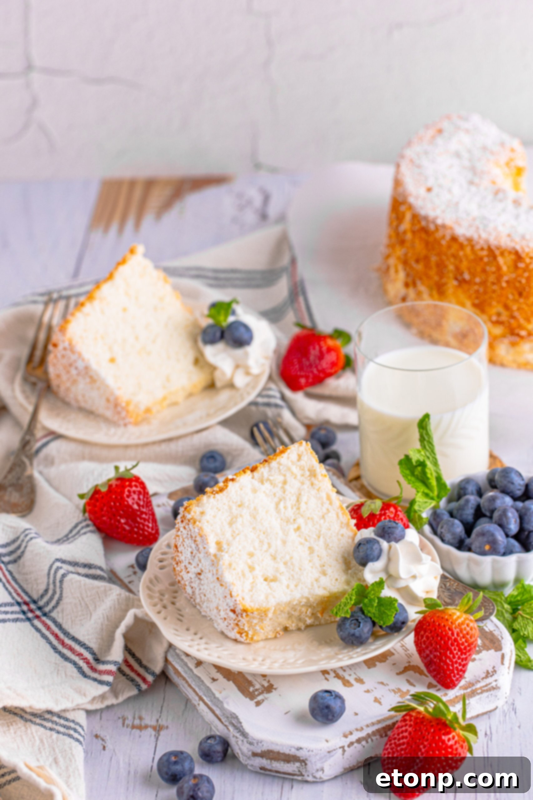 Two pieces of Angel Food Cake on a white plate with whipped cream, fresh berries, and mint