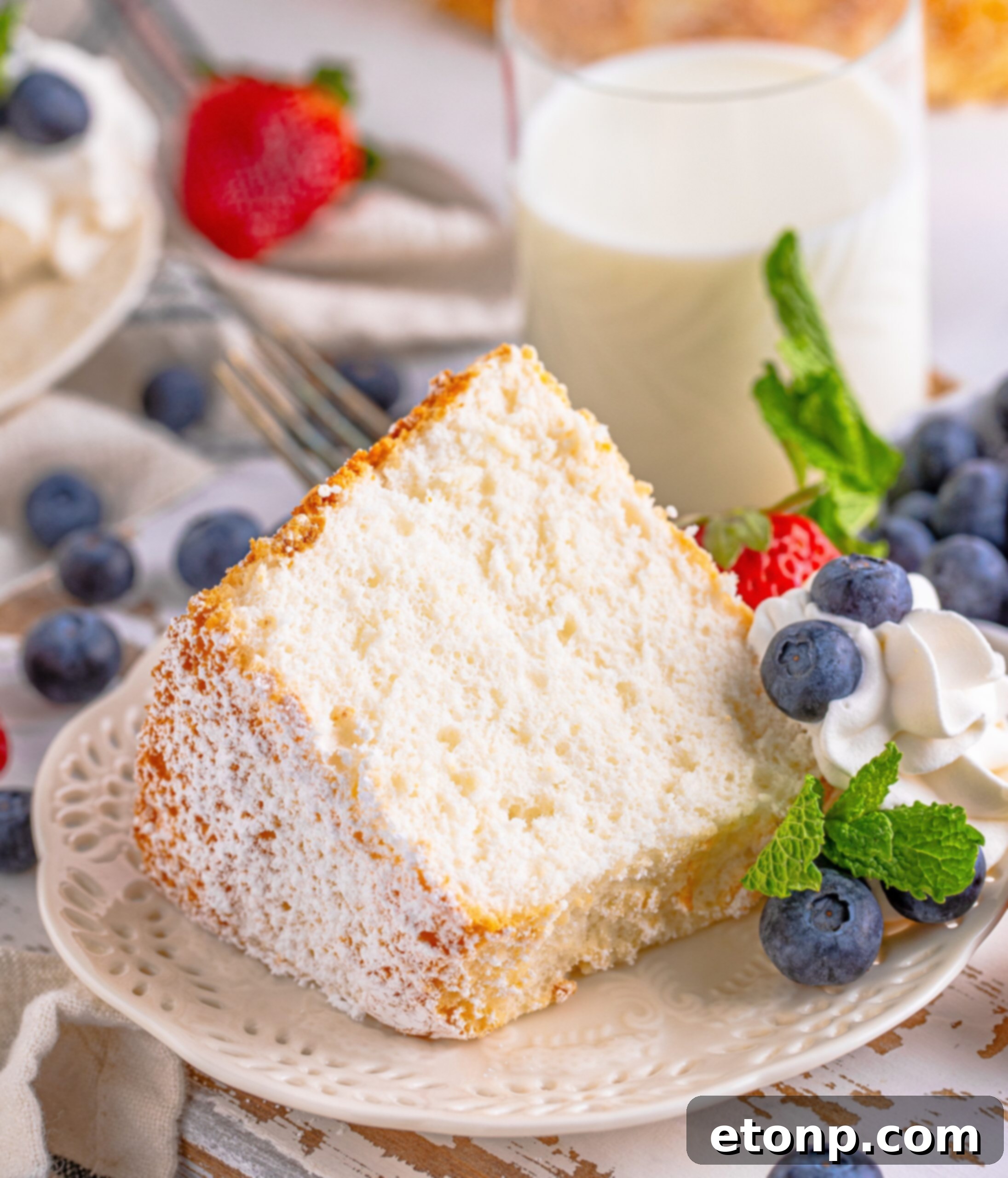 Angel Food Cake on a white plate with whipped cream, blueberries, strawberries, and mint