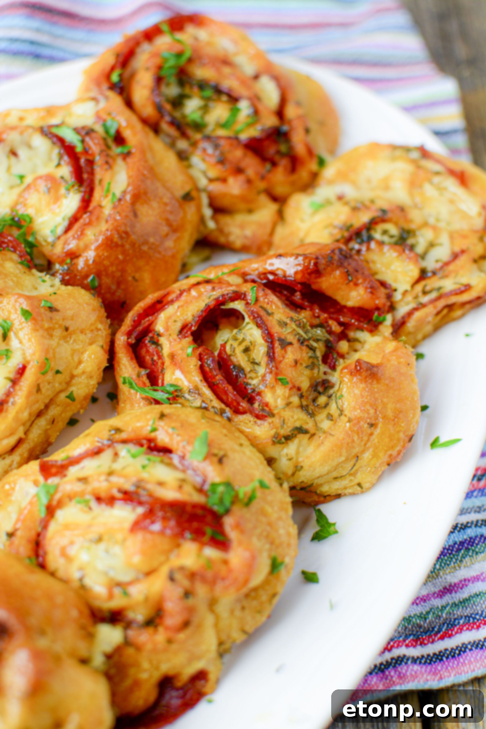 Pizza Swirls 3 Close-up overhead shot of a batch of golden, spiraled pizza pinwheels, revealing layers of cheese and pepperoni.