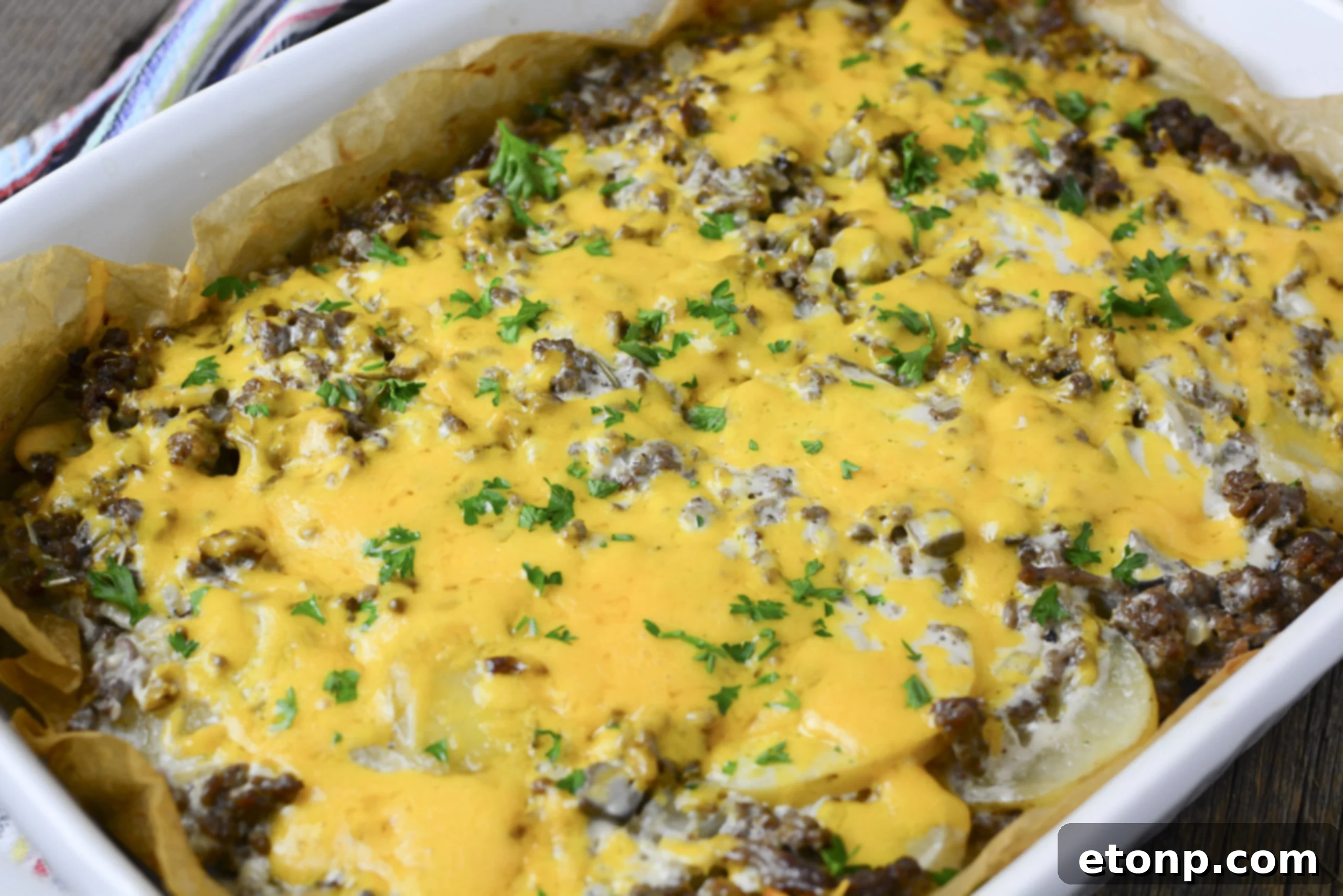 A generous serving of Ground Beef and Potato Casserole, smothered in melted cheese, in a white baking dish and topped with fresh parsley.