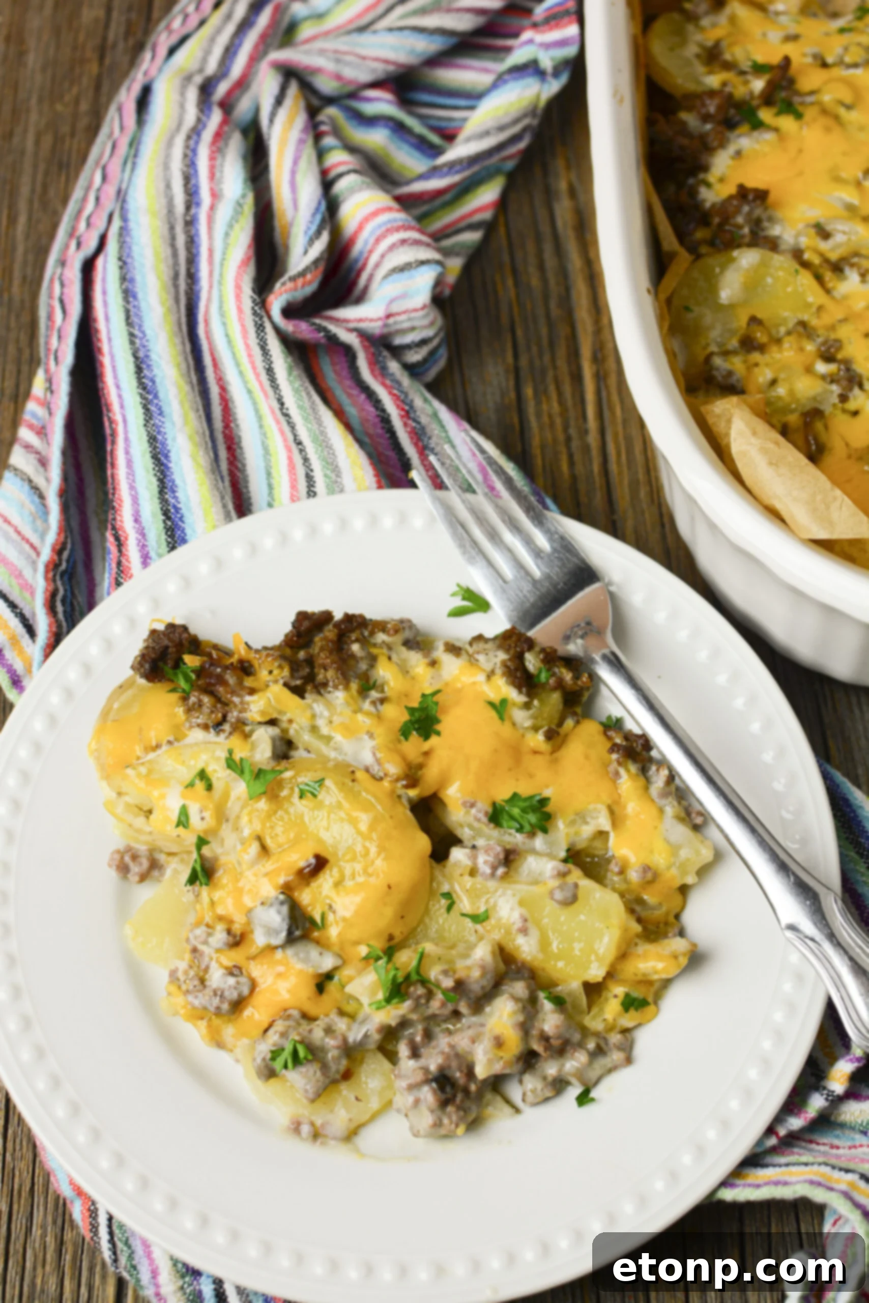 A portion of Cheesy Ground Beef and Potato Casserole on a white plate, topped with a sprig of fresh parsley.