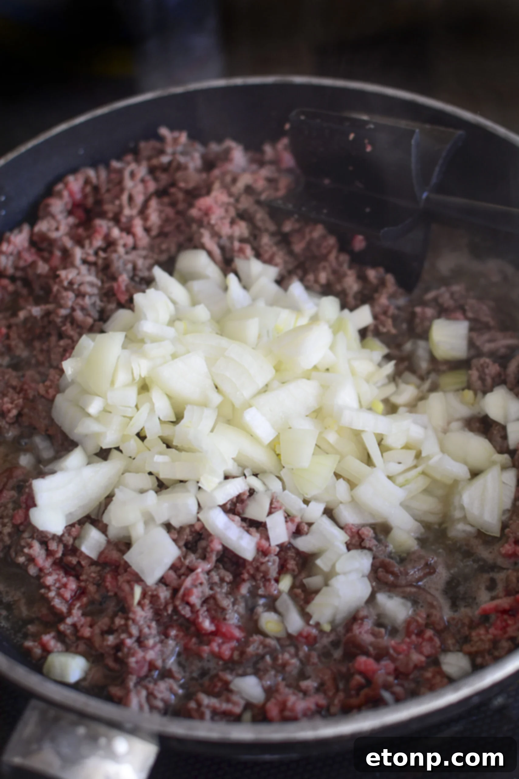 The process of layering ground beef into a casserole dish.