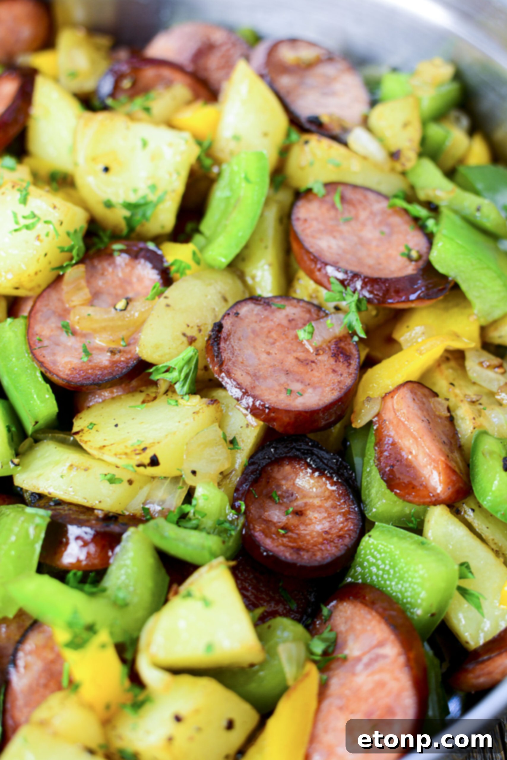 Close up view of sausage peppers and potatoes in a silvers skillet. 