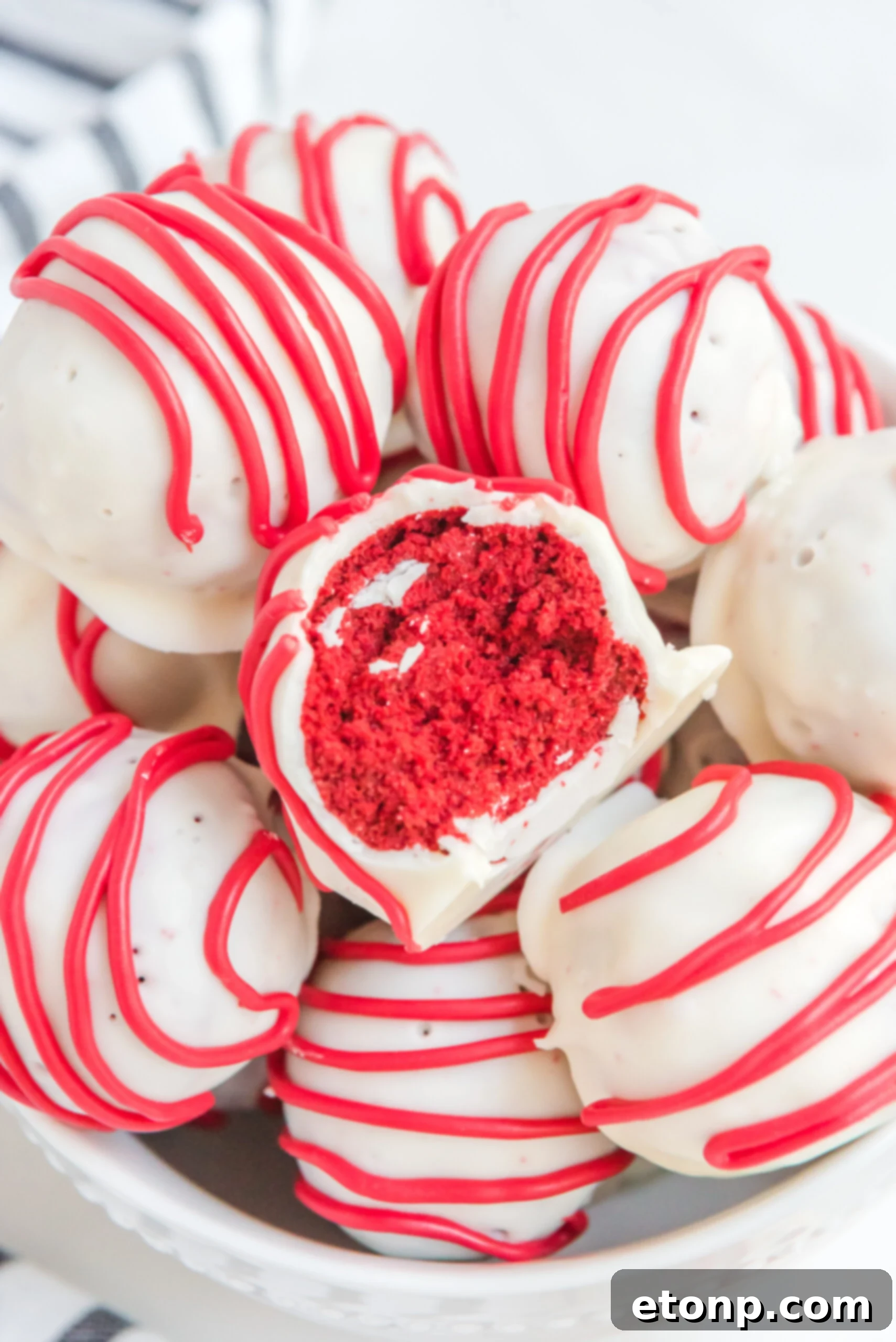 A red velvet cake ball stacked on top of other truffles with a bite removed showing the inside.