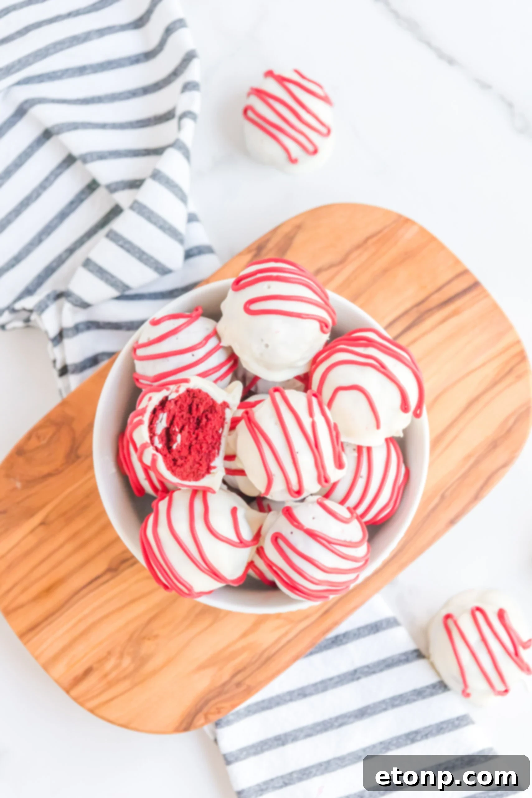 A red velvet cake ball stacked on top of other truffles with a bite removed showing the inside.