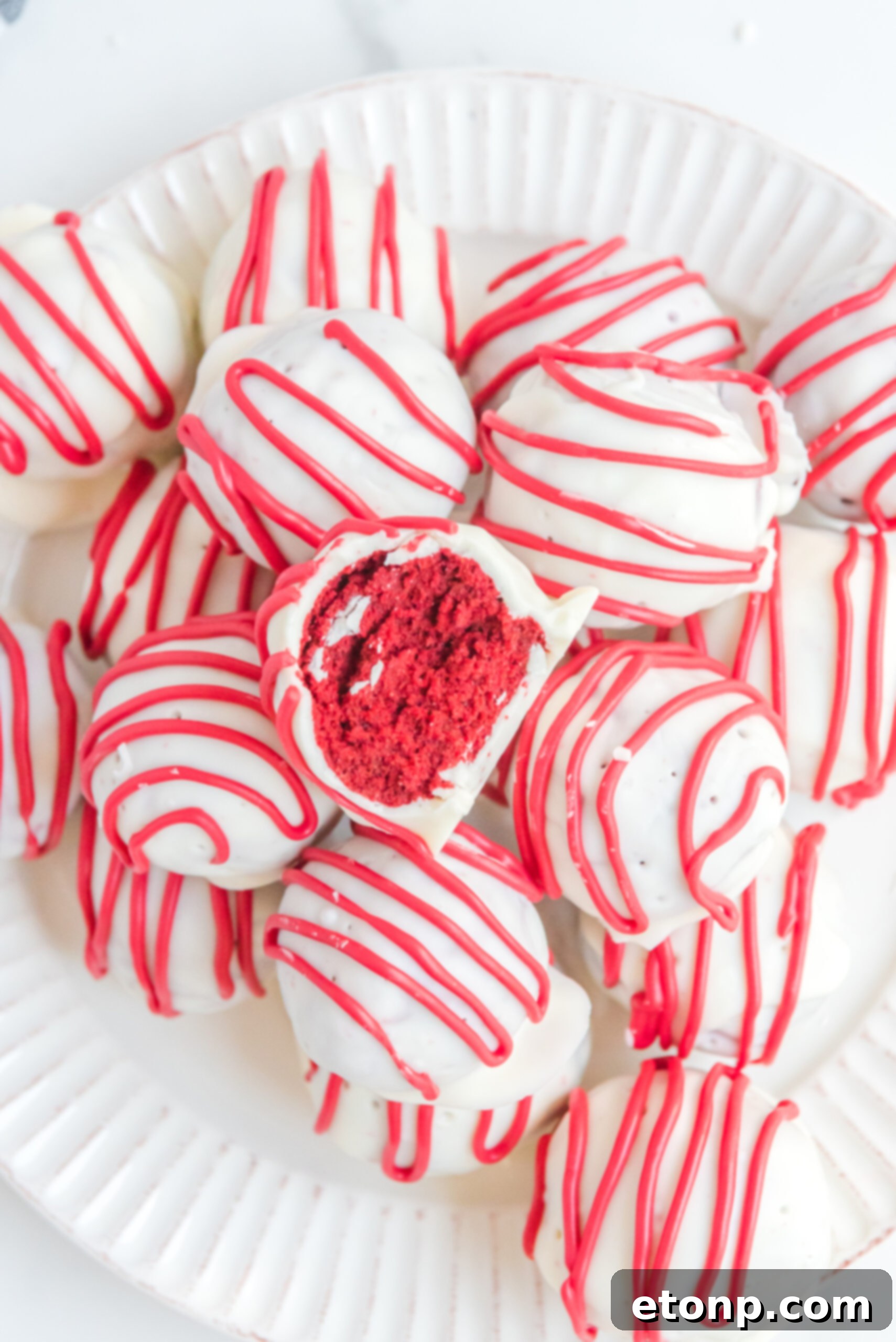 A red velvet cake ball stacked on top of other truffles with a bite removed showing the inside.