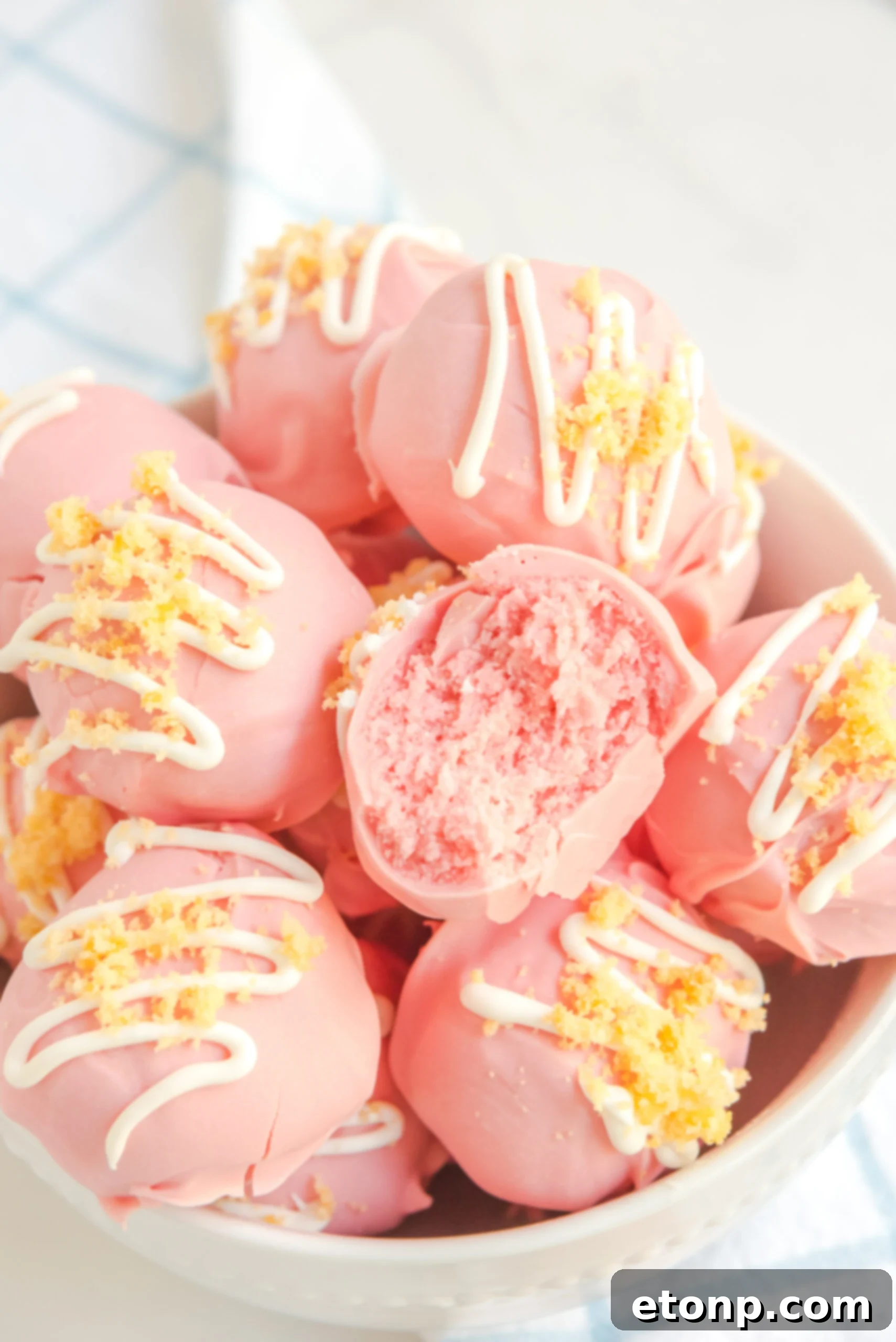 Stacked strawberry shortcake truffles in a white bowl, showcasing their pink hue and white chocolate drizzle.