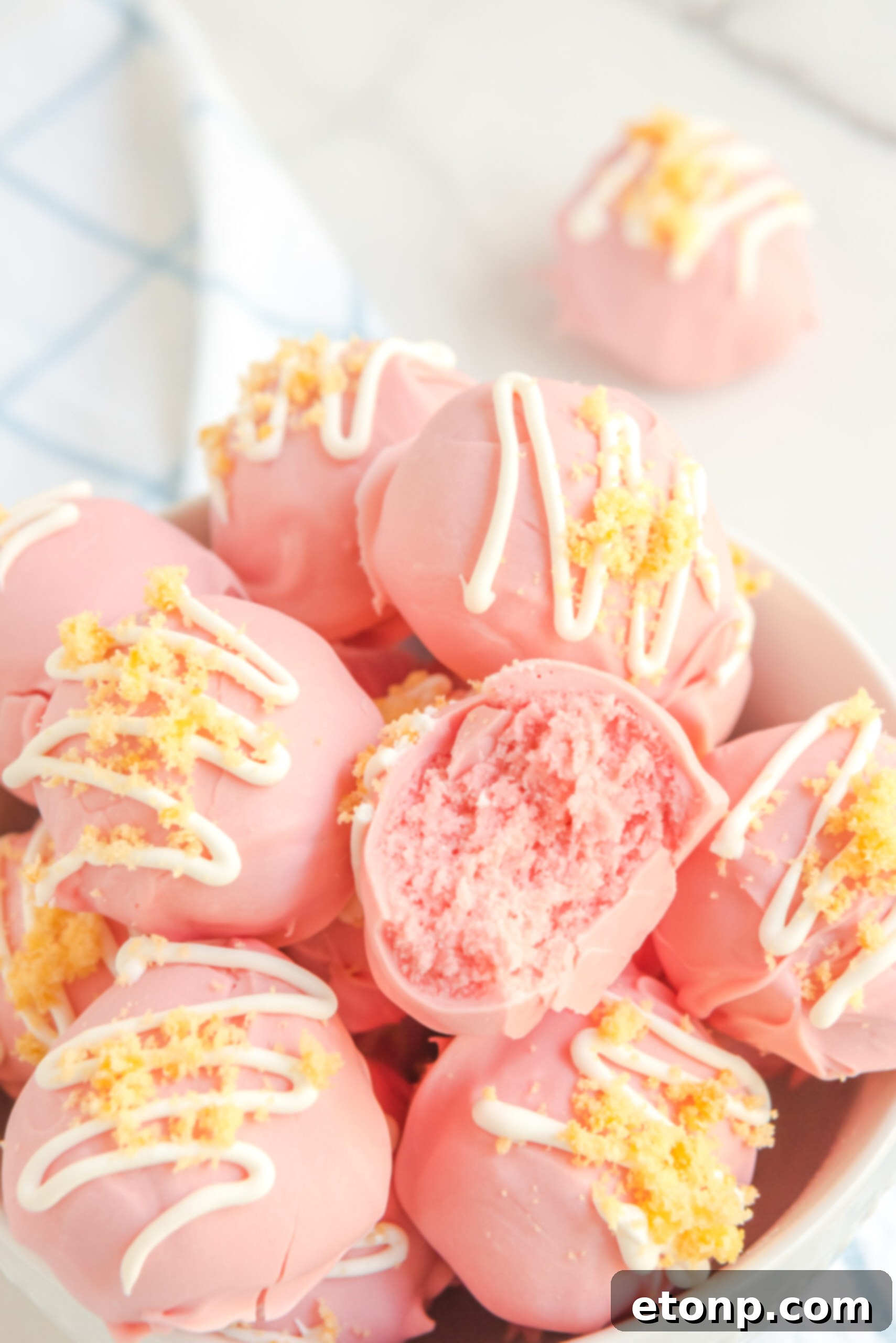 Strawberry shortcake truffles stacked in a white bowl, with one truffle having a bite taken out, revealing its moist interior.