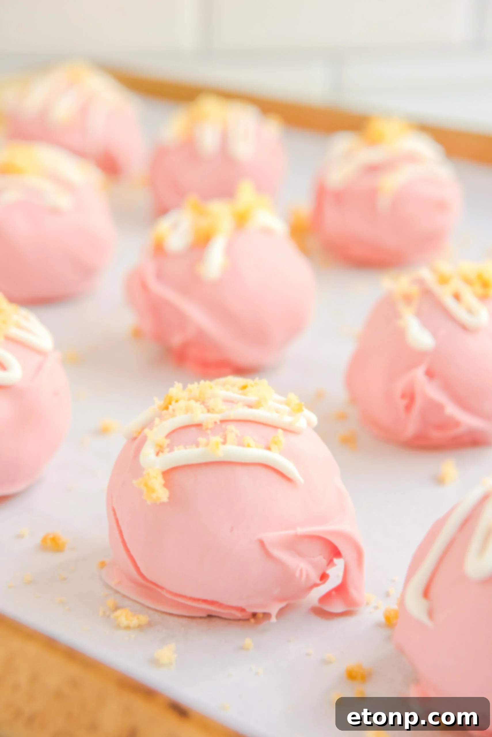 Strawberry truffles arranged on a baking tray, topped with elegant white chocolate drizzles.