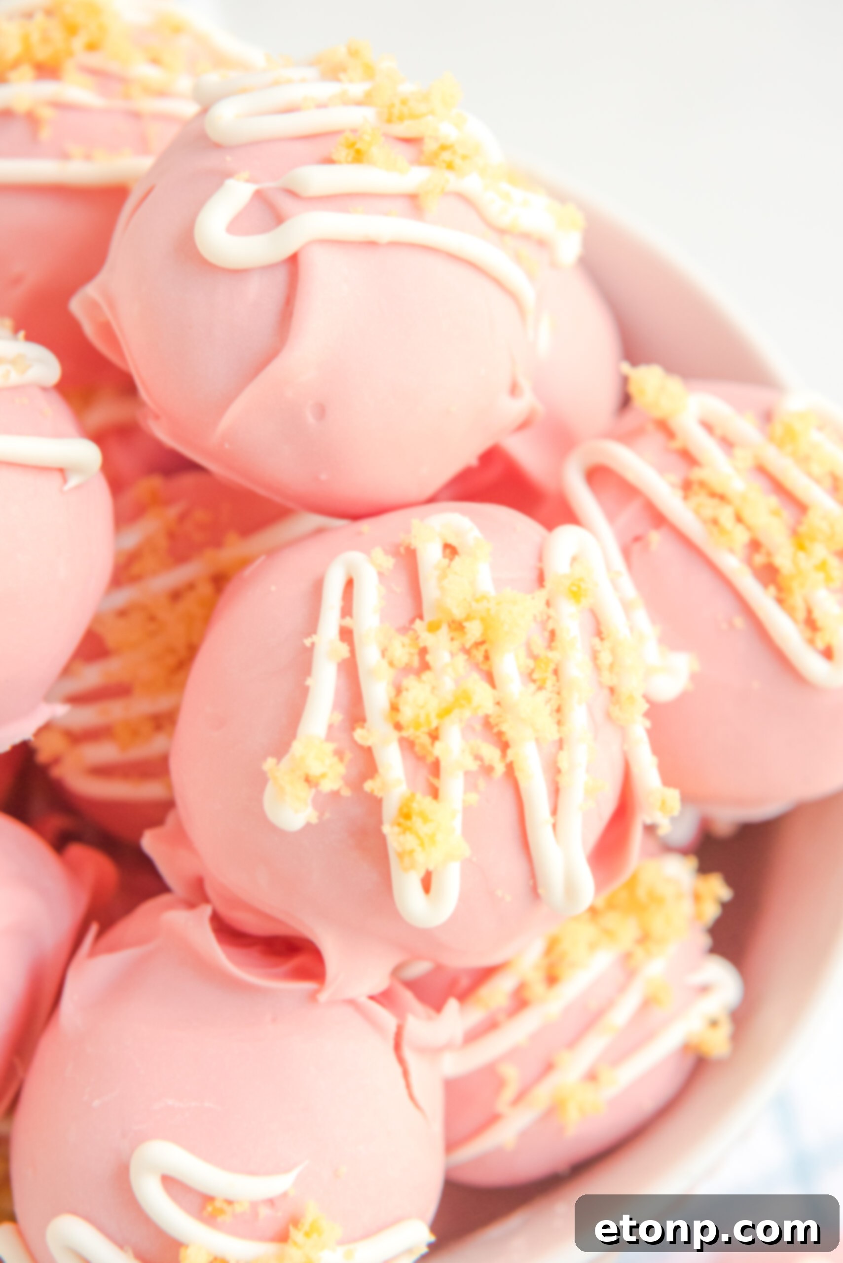 Close-up of strawberry shortcake truffles stacked in a pristine white bowl, highlighting their delicate toppings.