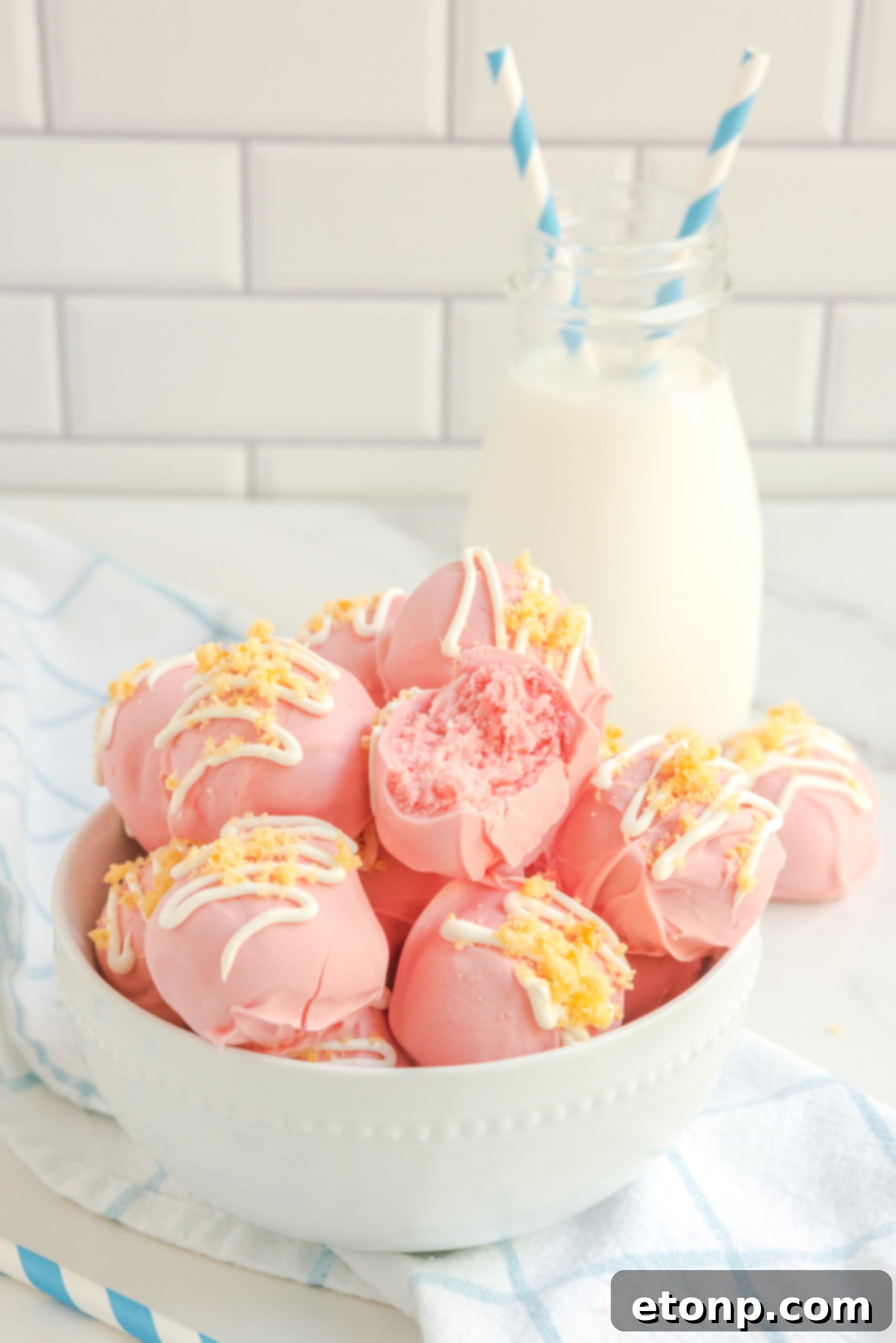 A bowl of strawberry shortcake truffles with a glass of milk and blue and white straws in the background, creating a whimsical scene.