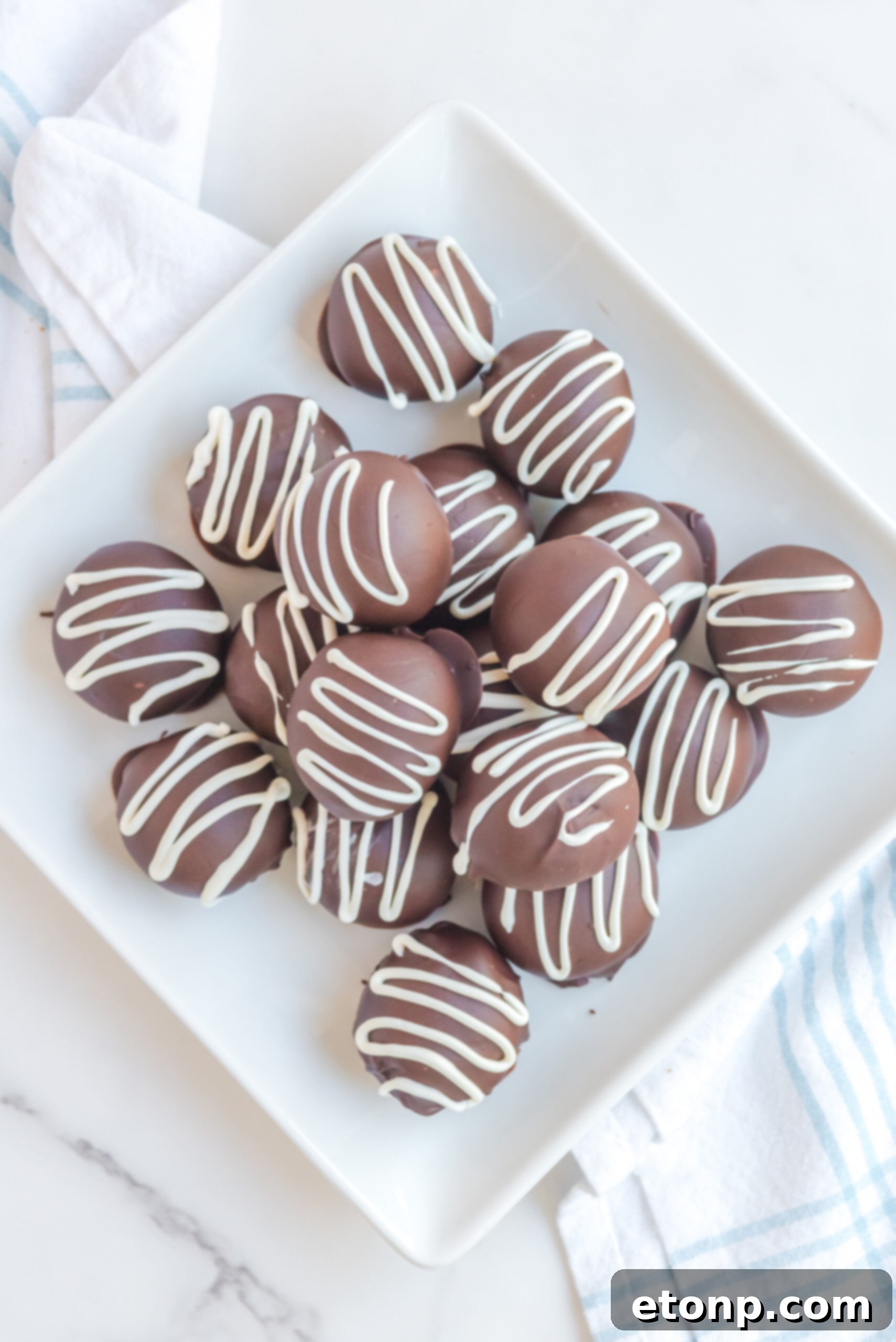 Decadent Brownie Truffles 12 Brownie Truffles are artfully stacked on a white plate, with the soft focus of brownies in the background, creating a harmonious and tempting dessert presentation.