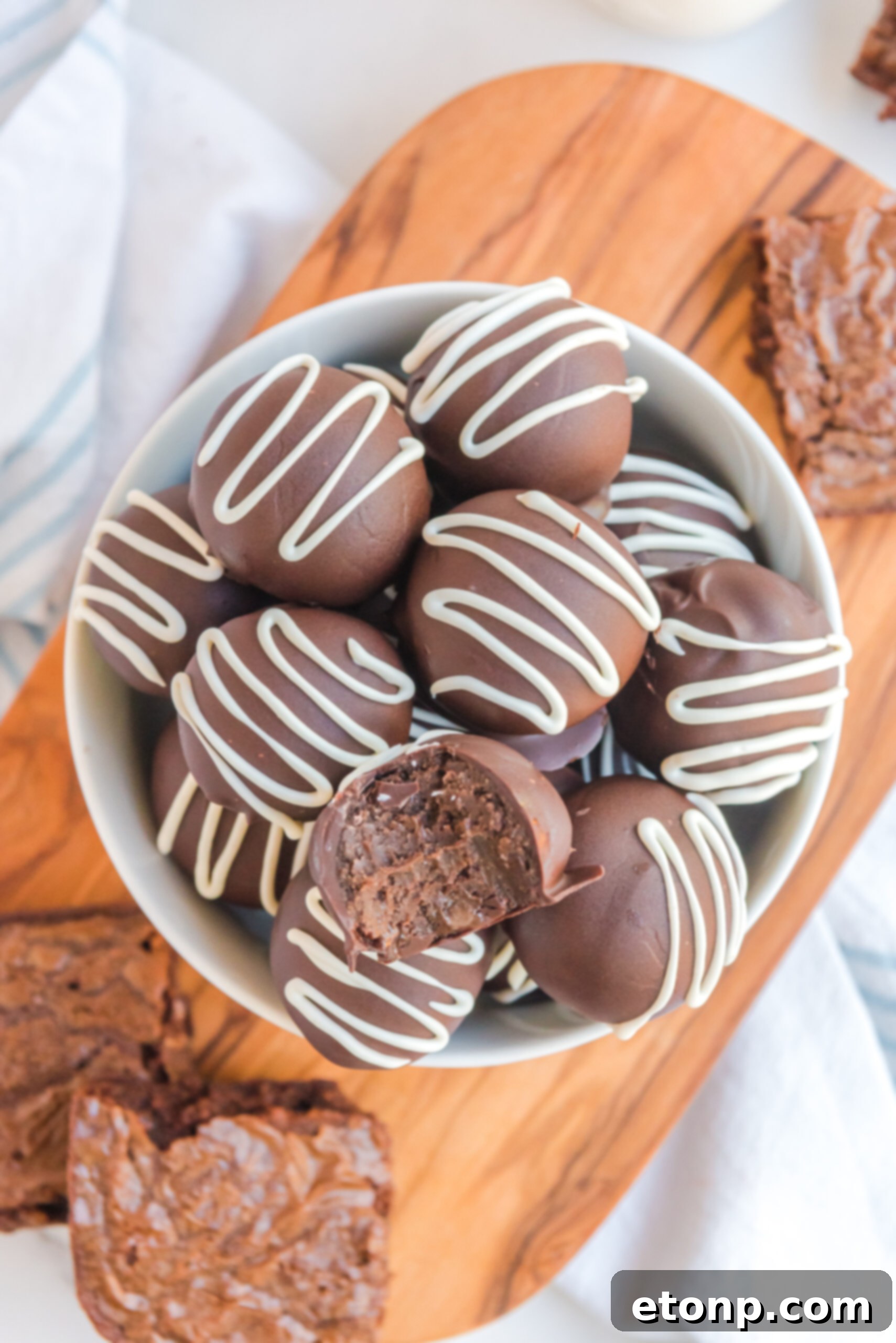Decadent Brownie Truffles 16 Brownie Truffles, stacked neatly in a white bowl, with a tempting bite taken from the top truffle, inviting further indulgence.
