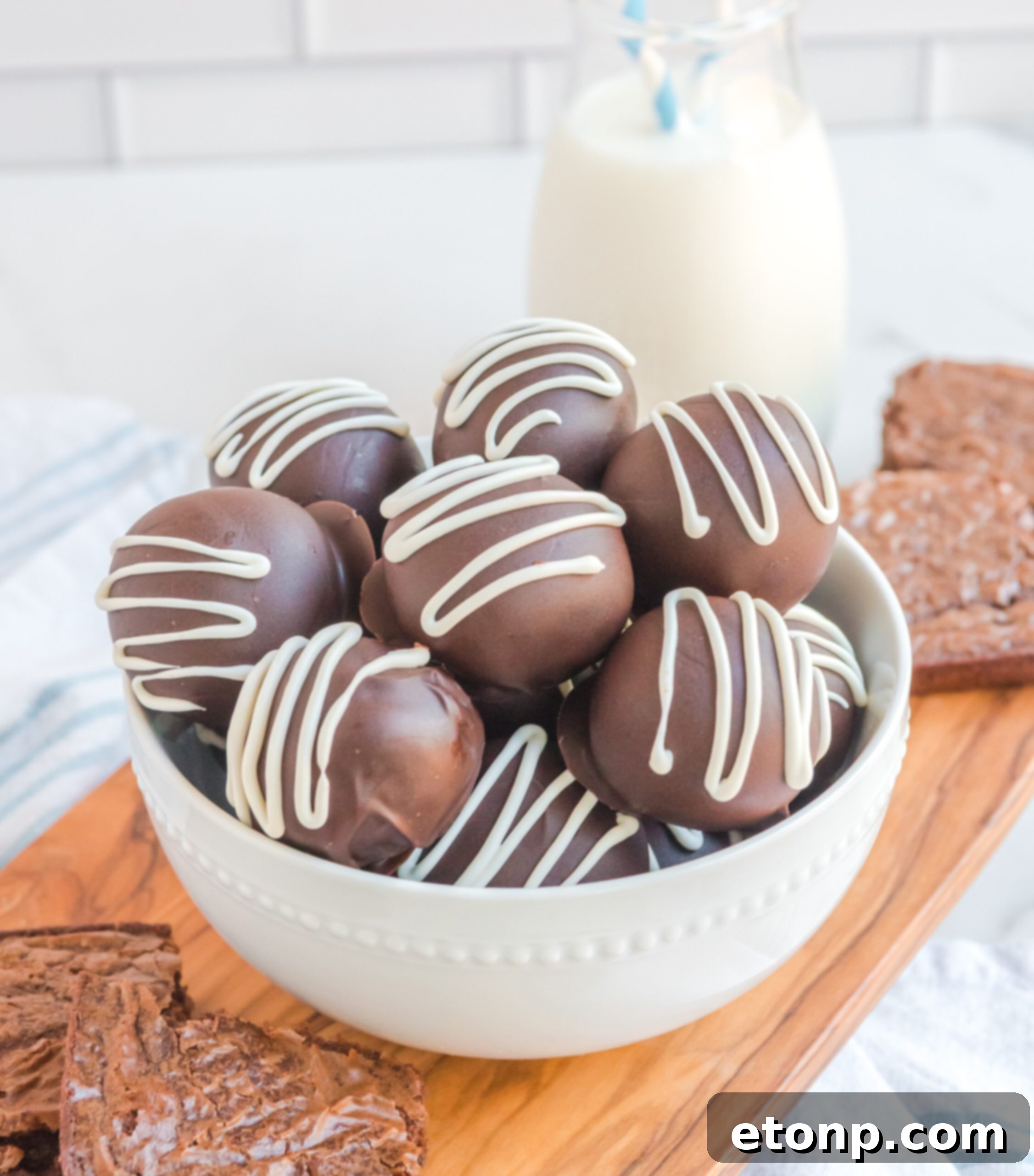 Decadent Brownie Truffles 17 Brownie Bite Truffles are elegantly presented in a white bowl, with a refreshing glass of milk positioned gracefully behind them, suggesting a perfect pairing for this delightful dessert.