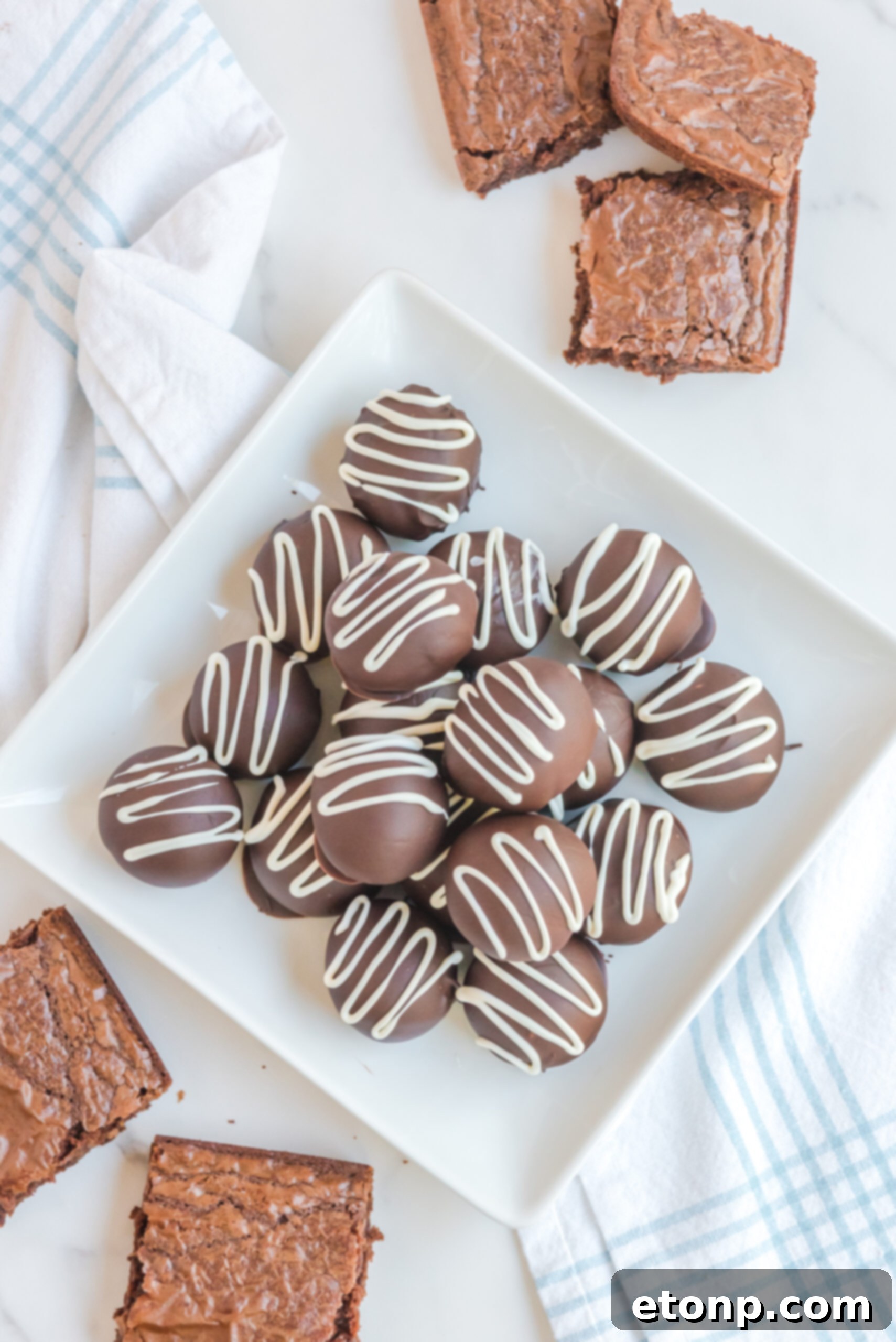 Decadent Brownie Truffles 4 An artistic arrangement of Brownie Truffles, meticulously stacked on a white plate, with a soft focus on additional brownies in the background, creating a visual feast.