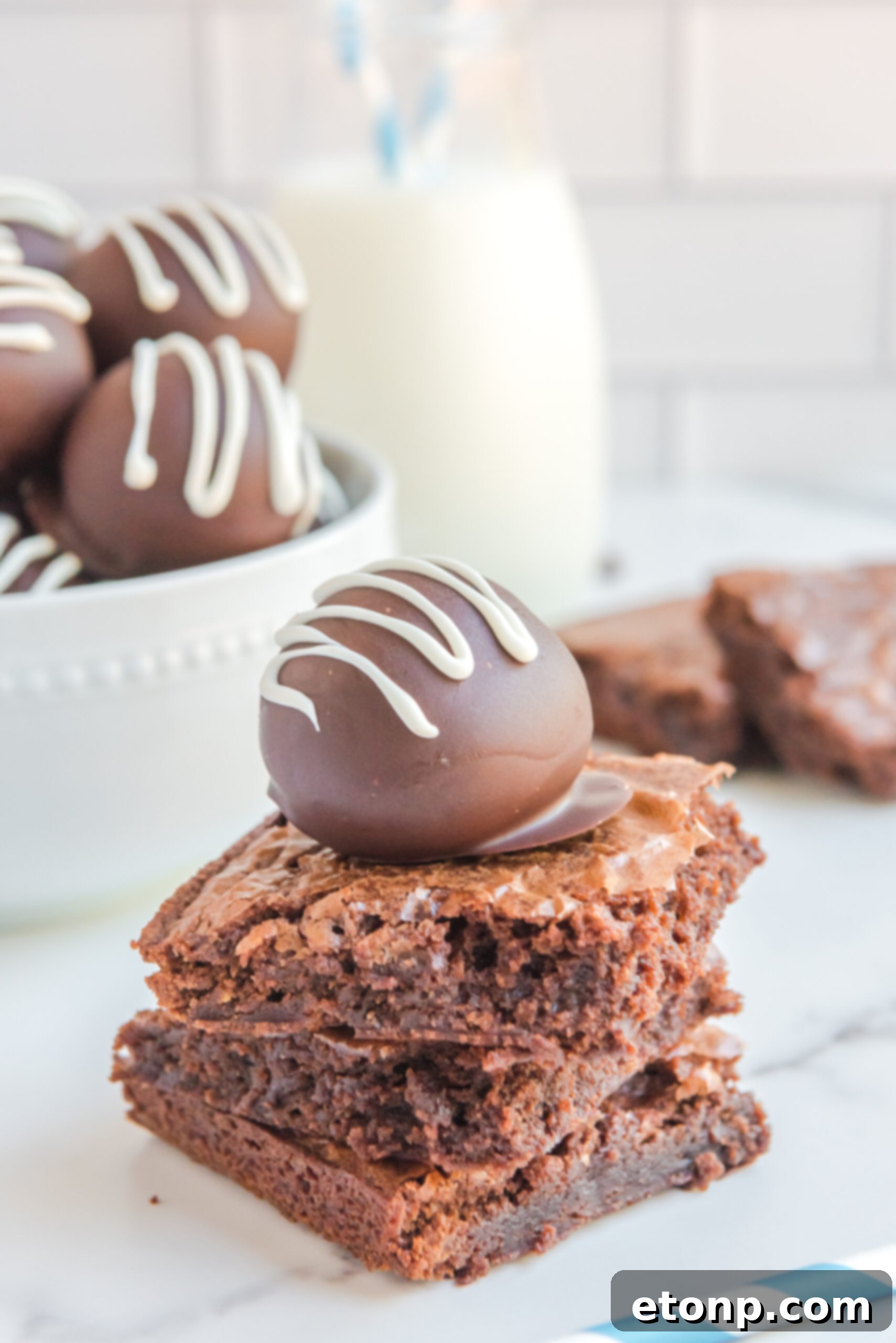 Decadent Brownie Truffles 6 A single, perfectly formed Brownie Truffle rests atop a trio of rich, fudgy brownies, showcasing its alluring texture and inviting appearance.