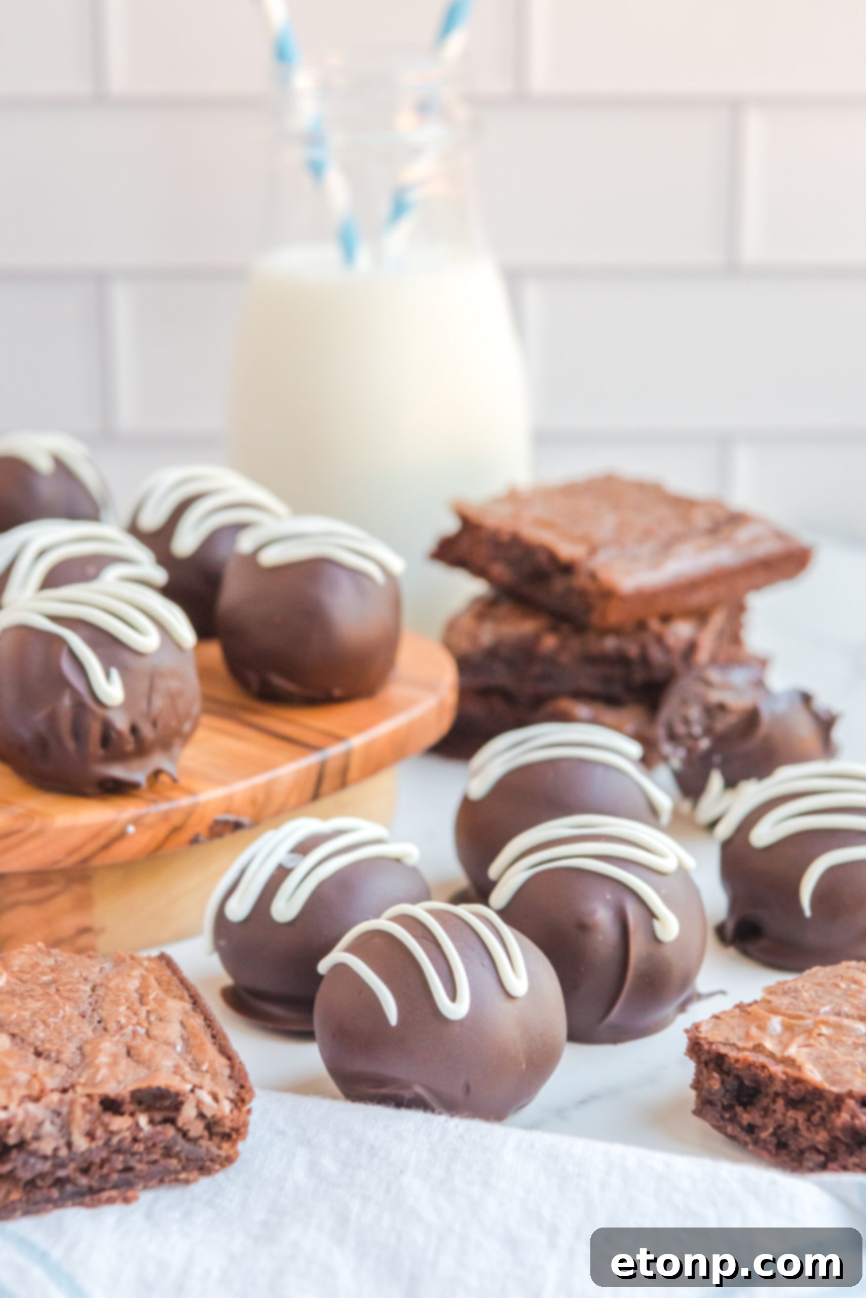 Decadent Brownie Truffles 9 A stunning display of Brownie Bite Truffles adorning a white table, surrounded by stacks of brownies, creating an abundant and irresistible tableau.
