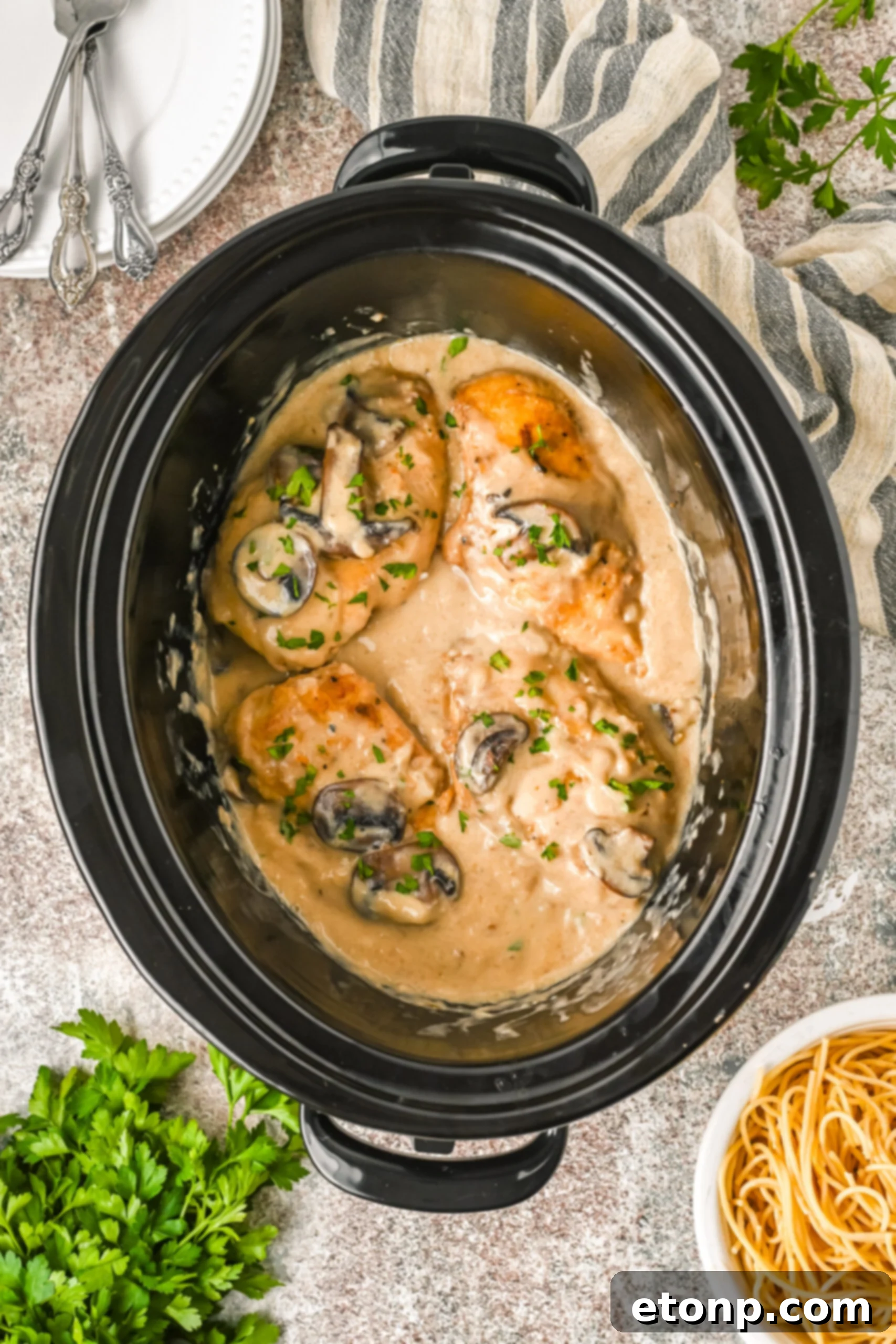 Overhead shot of slow cooker chicken marsala in the slow cooker inner pot topped with fresh parsley. 