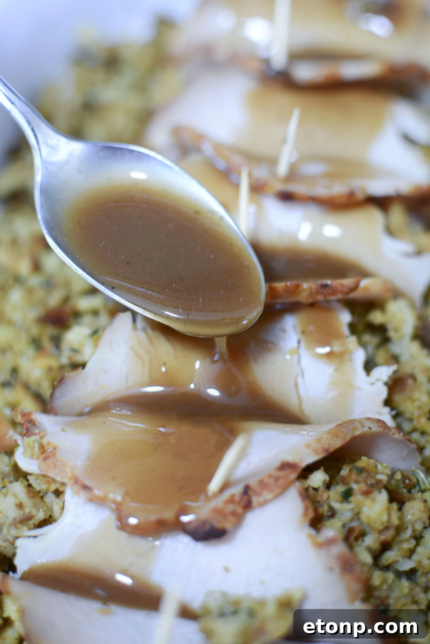  A silver spoon spooning gravy over turkey stuffing rolls. 