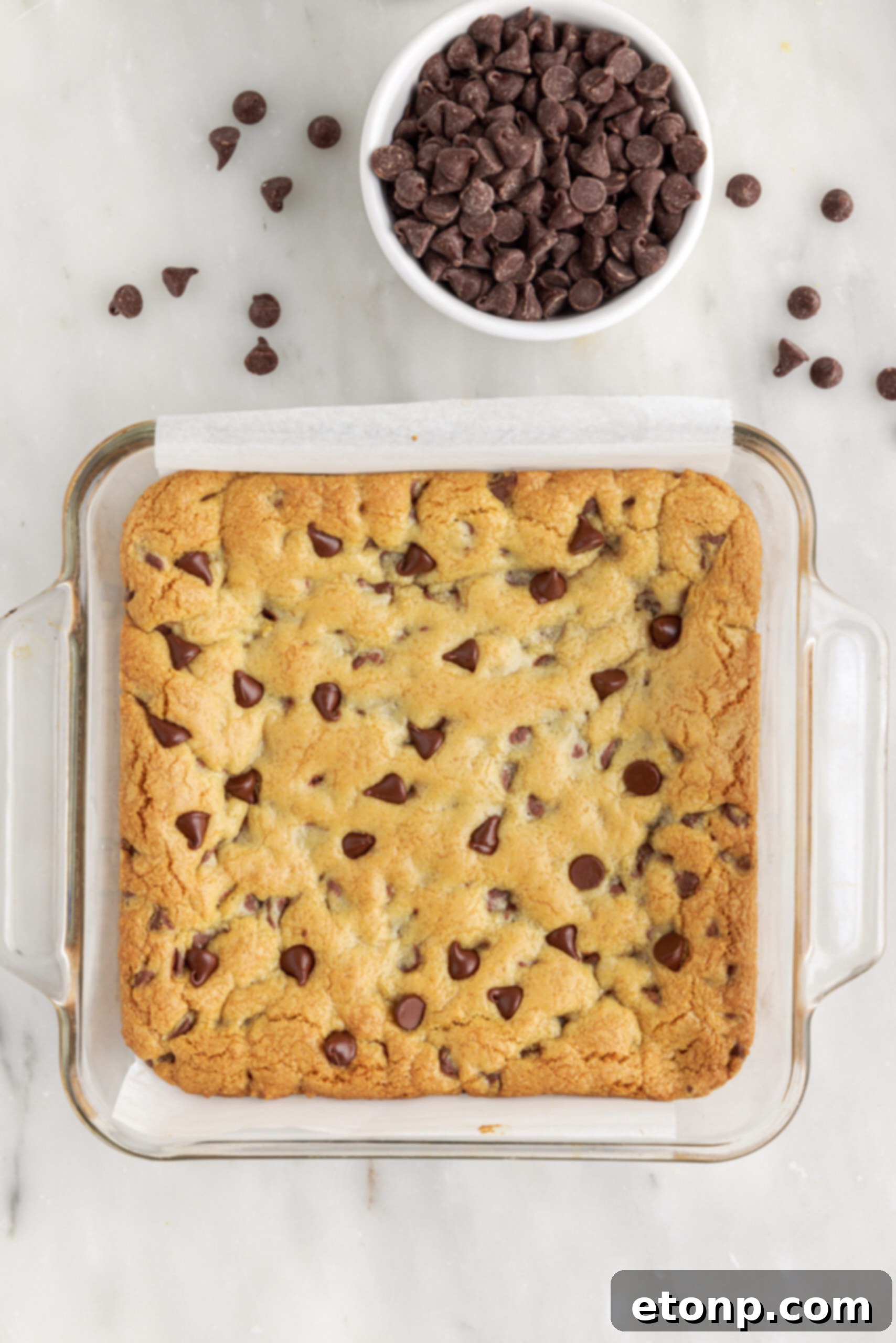 A spatula gently folding chocolate chips into the prepared cookie dough in a mixing bowl.