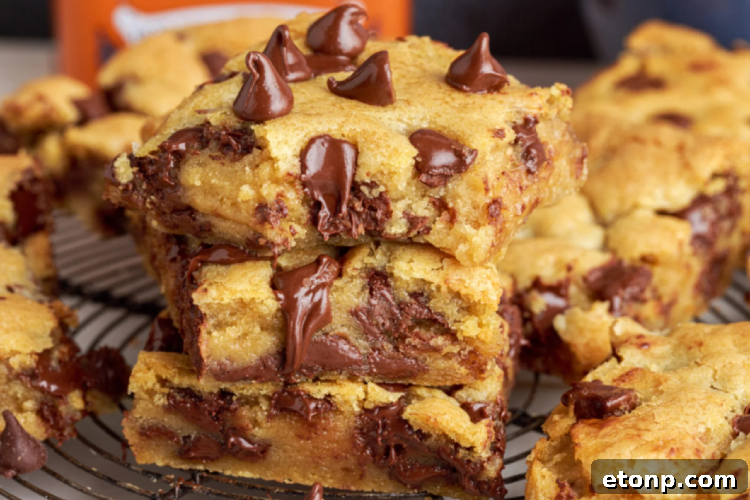 Side view of three stacked gooey chocolate chip cookie bars, with a bite taken from the top one, revealing the soft, chocolate-filled interior.
