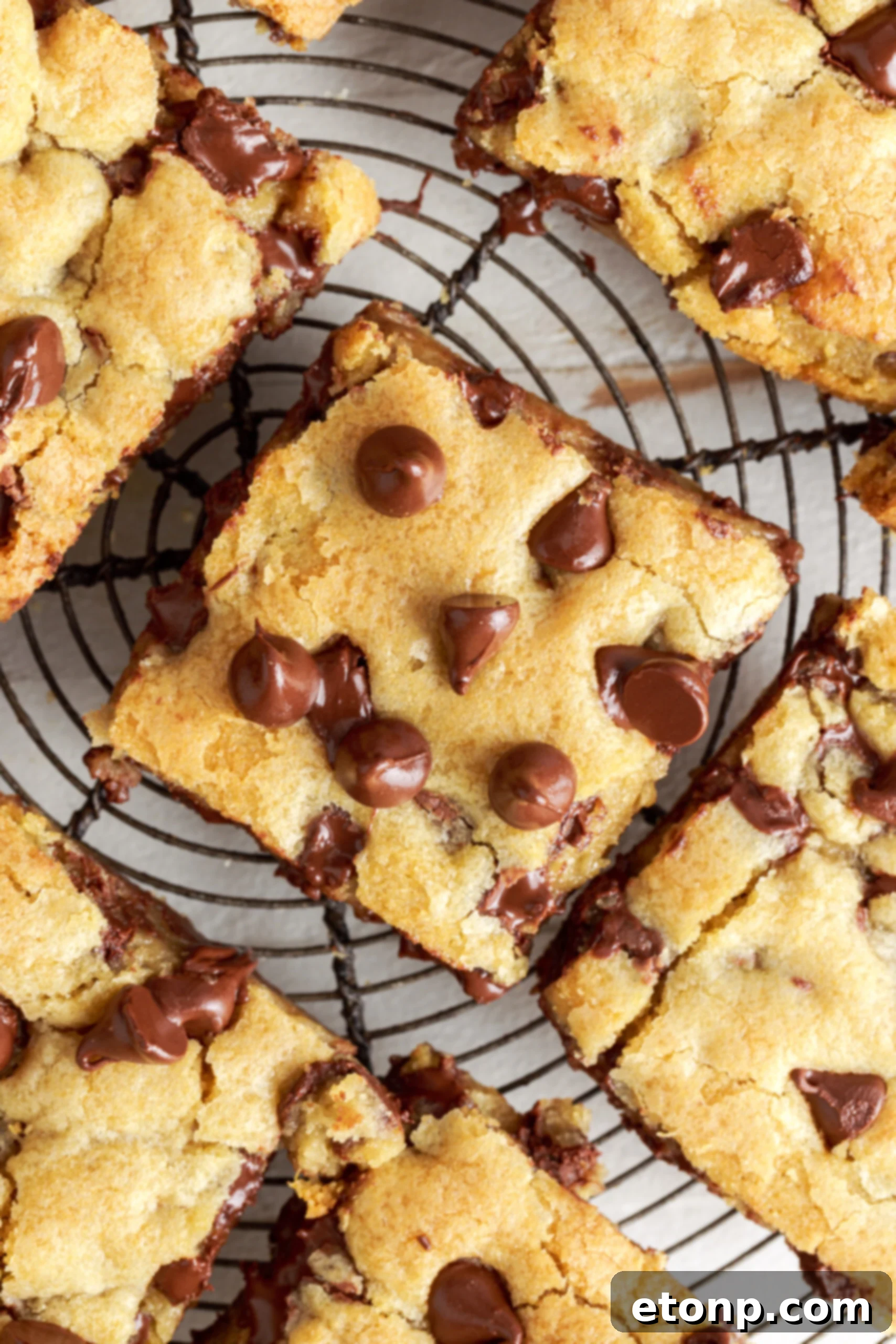 Close-up overhead view of a gooey chocolate chip cookie bar on a wire rack, highlighting the melted chocolate chips and soft interior.