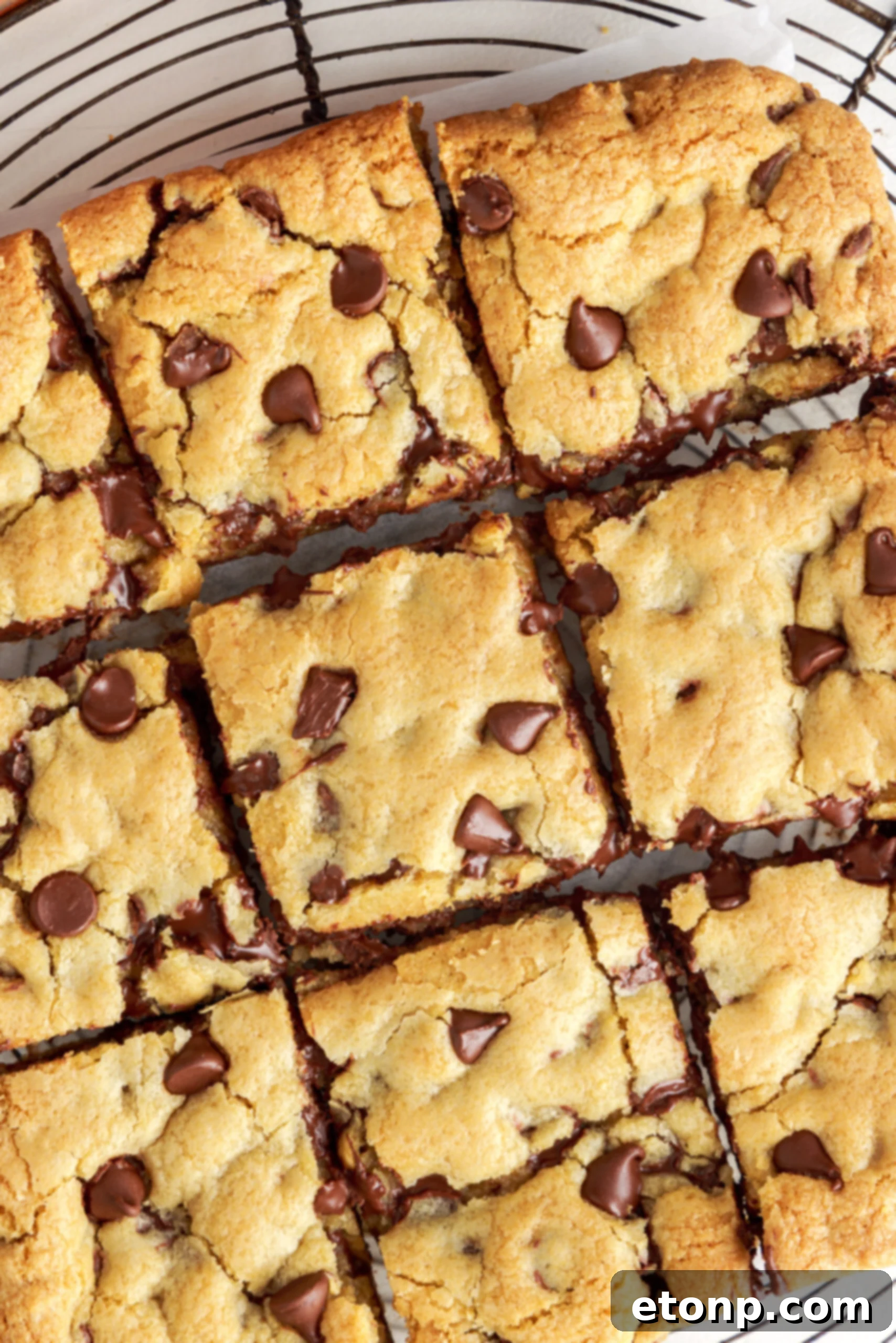 Overhead view of nine gooey chocolate chip cookie bars, perfectly cut and arranged on a wire rack to cool.