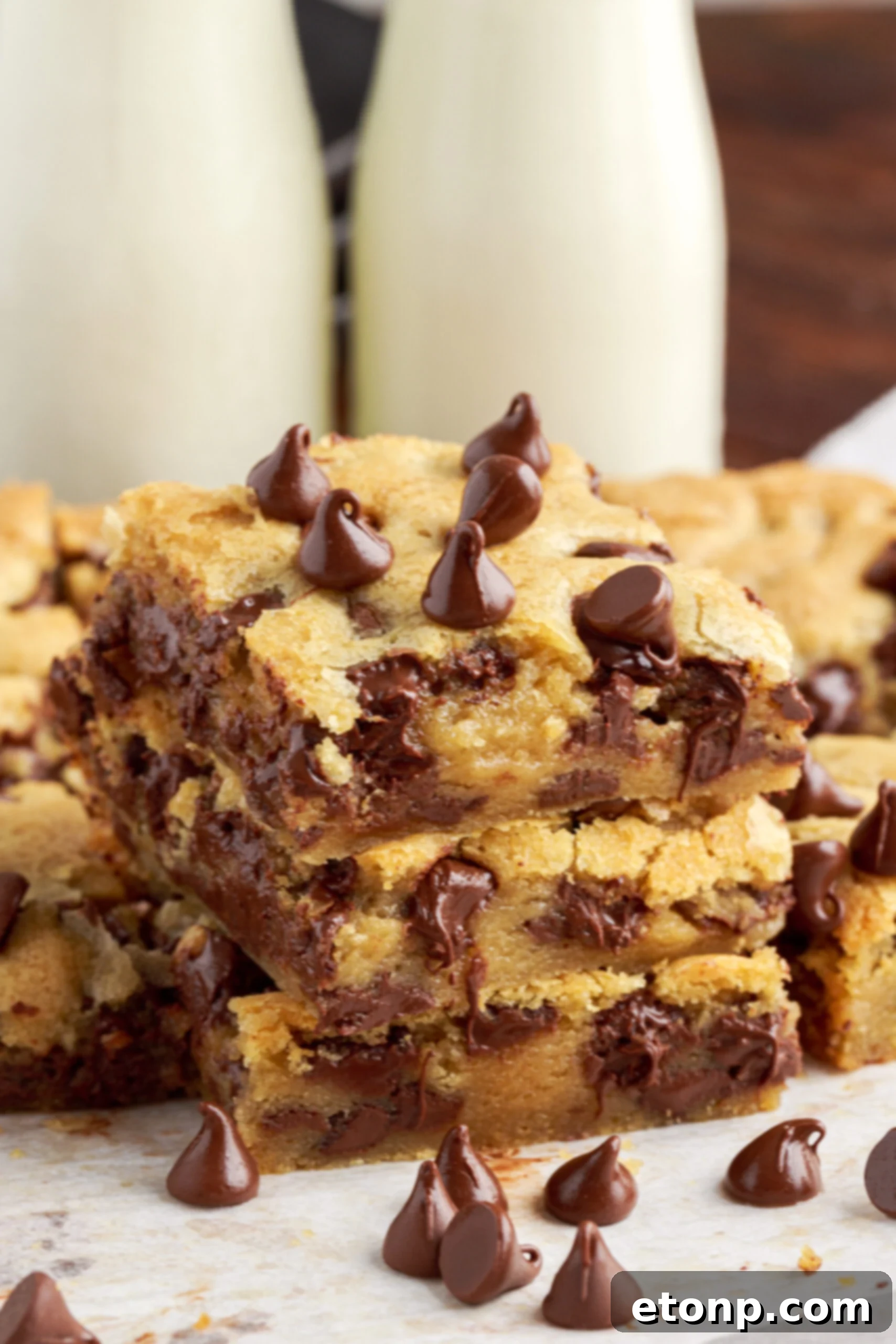 Close up view of a freshly baked gooey chocolate chip cookie bar, showing its texture and generously melted chocolate chips on a wire rack.