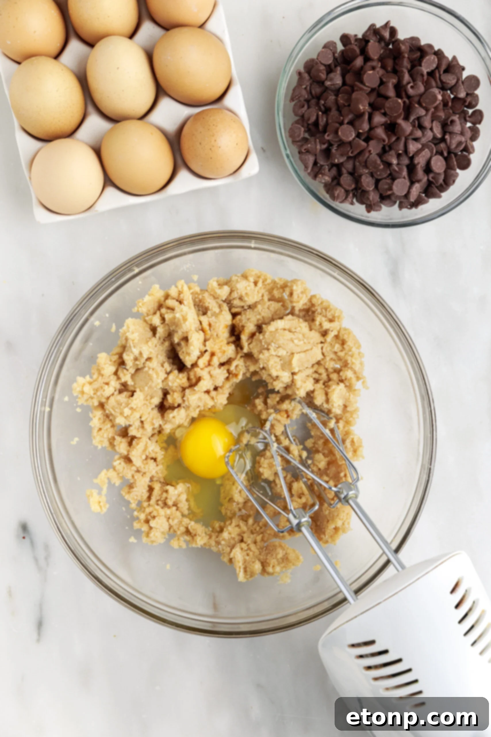 Unbaked chocolate chip cookie dough mixture in a large glass mixing bowl.