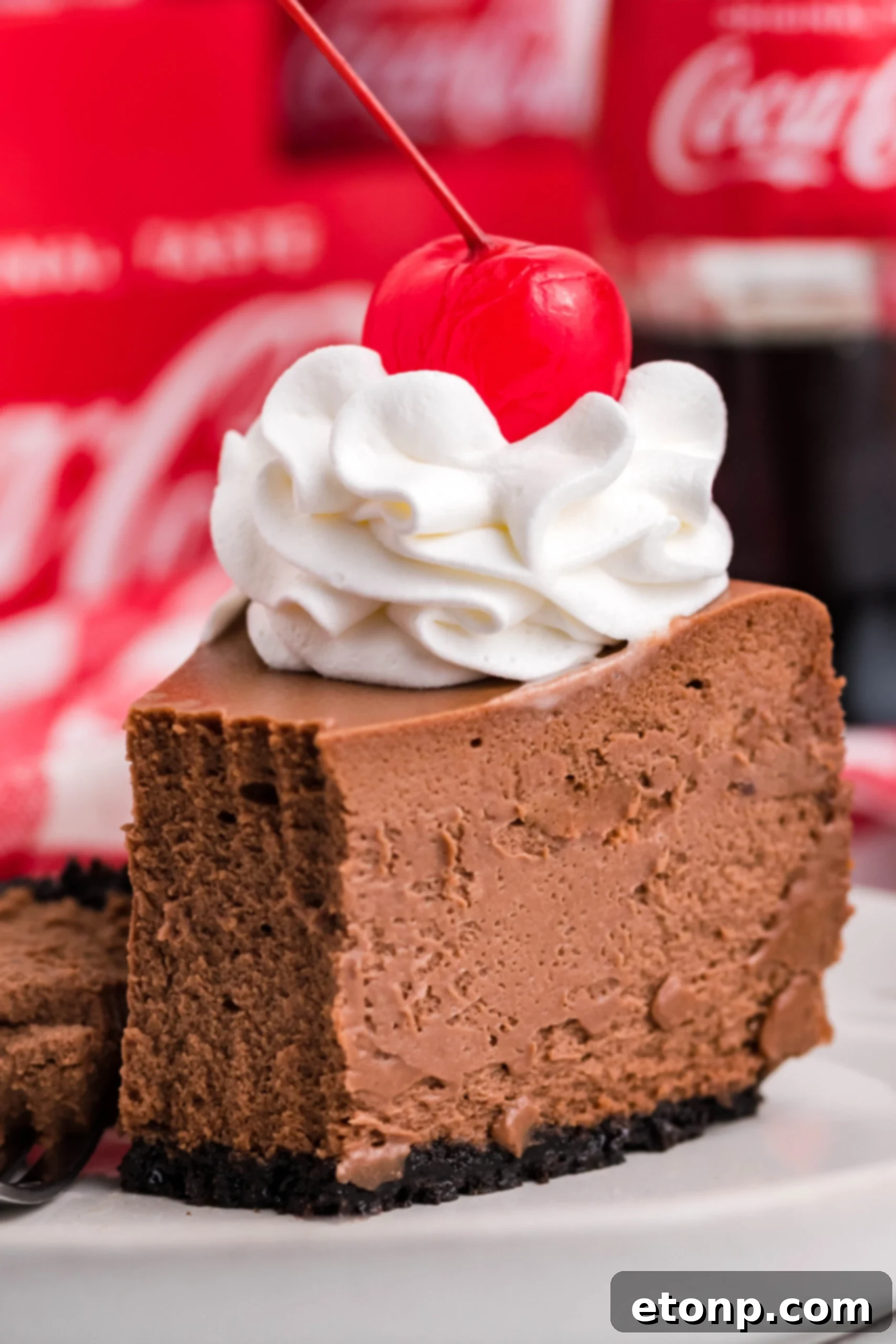 Decadent Coca-Cola Cheesecake 6 Coca-Cola Cheesecake slice on a white plate topped with whipped cream and a cherry